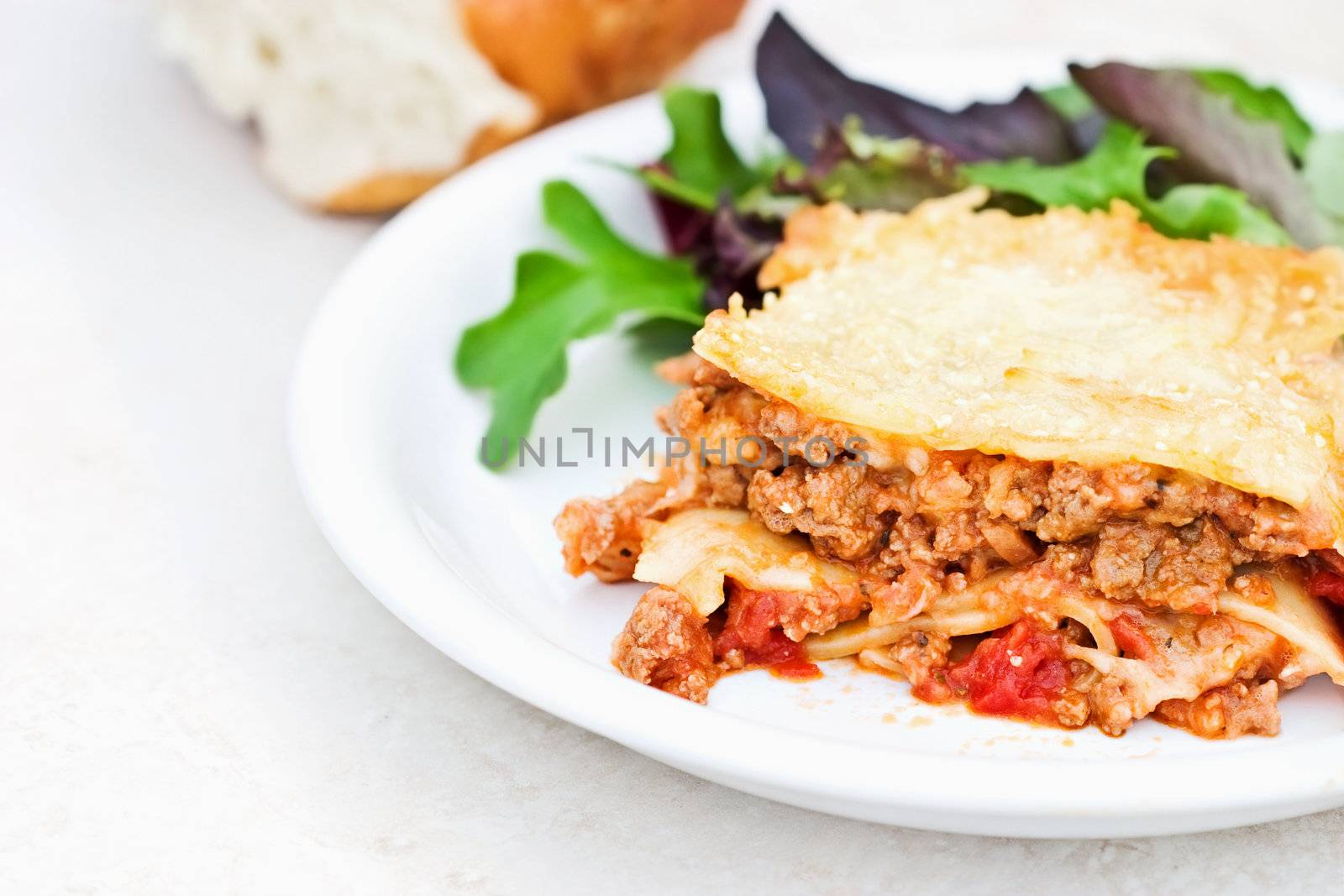 Meat lasagna with herb and mint salad and bread. Shallow DOF with focus on lasagna.