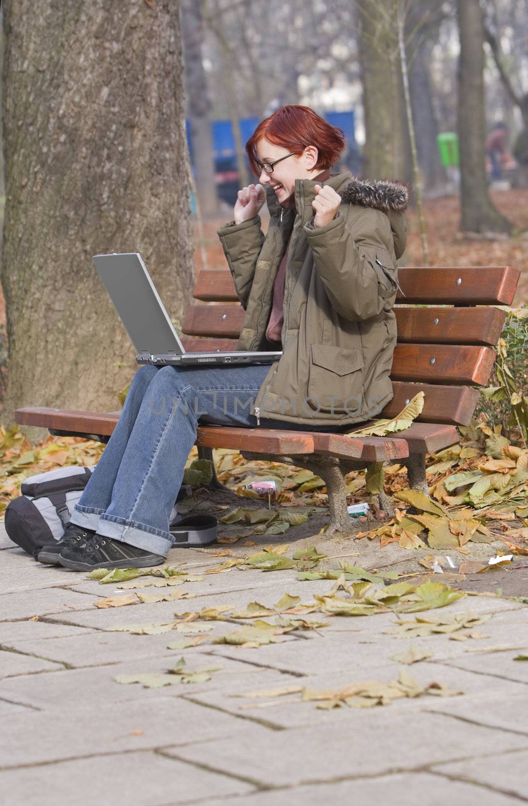 Happy redheaded girl with a laptop in an autumn park.