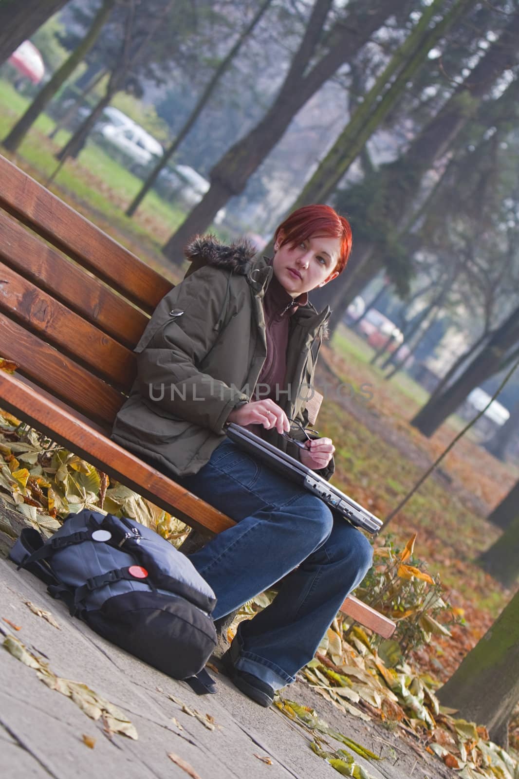 Lonely girl with a laptop siting on a bench in an autumn park.
