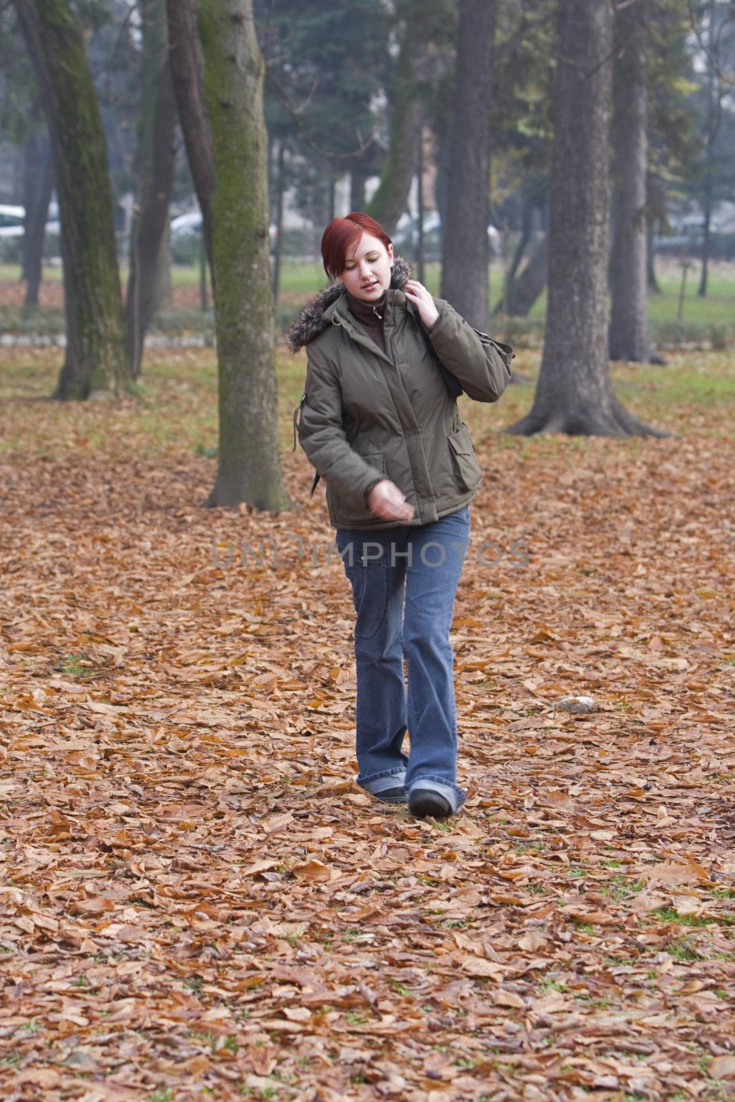 Redheaded backpacker girl walking in an autumn park.
