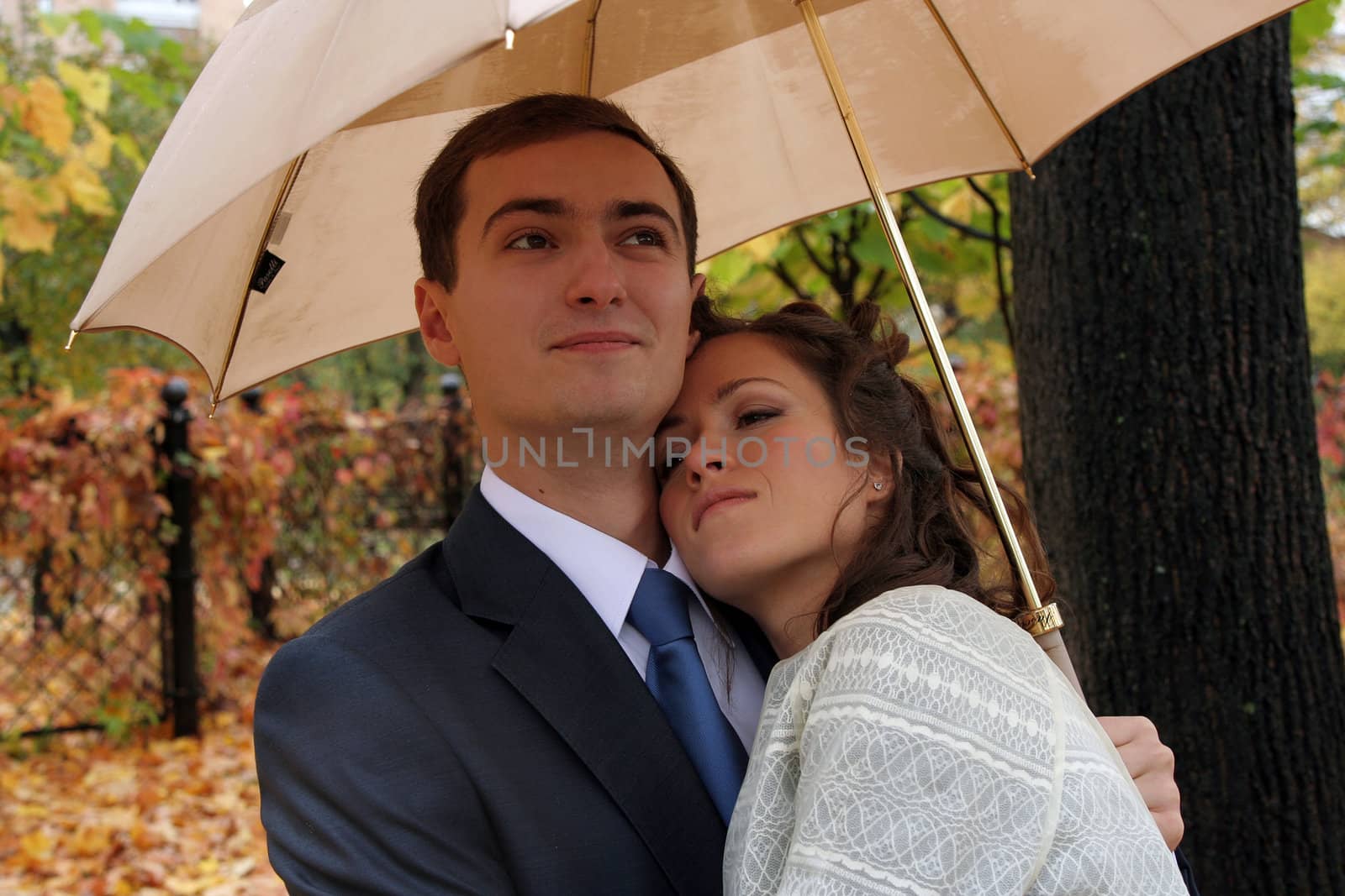 The groom and the bride under an umbrella walk in park in the autumn