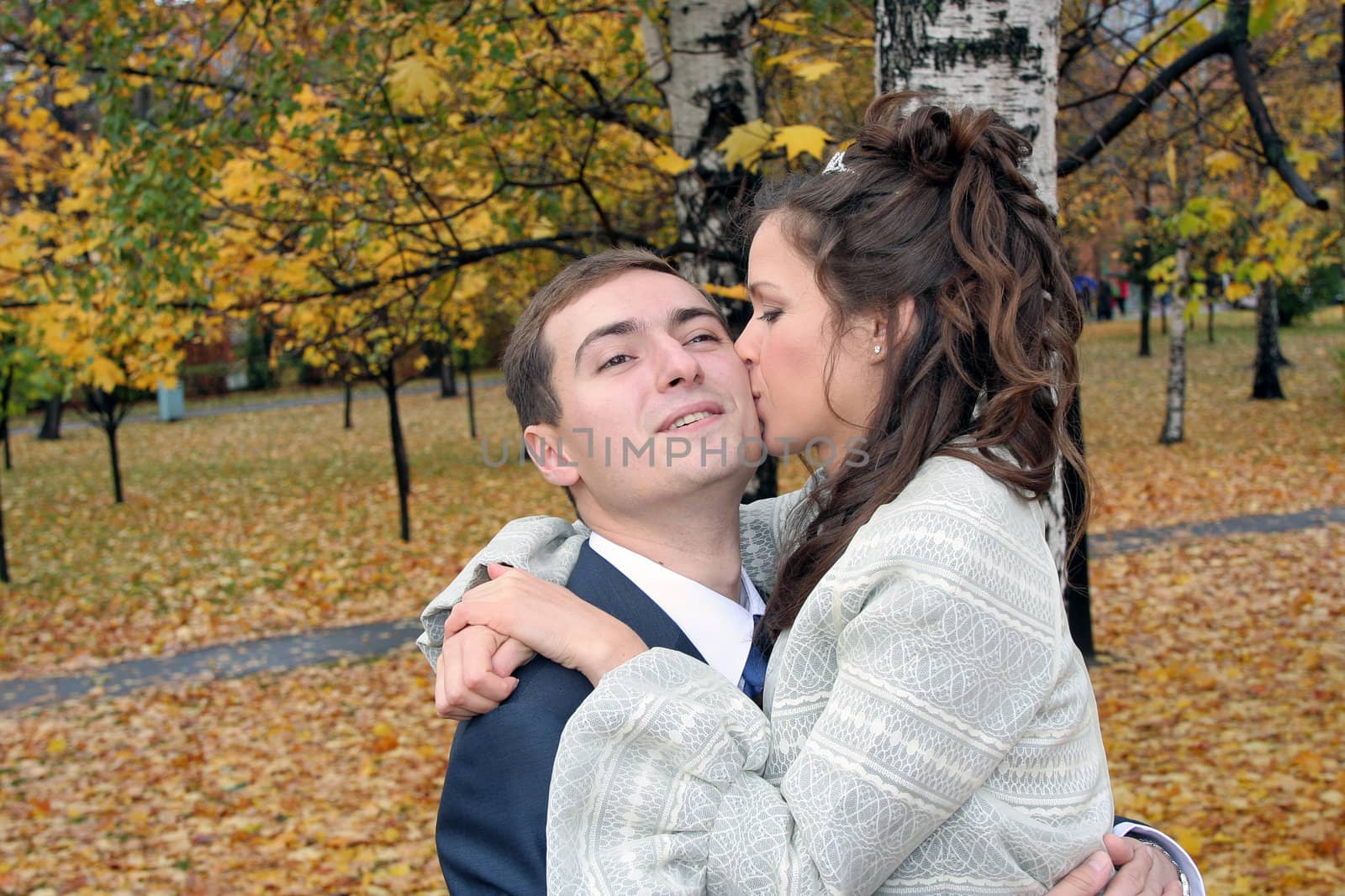 The bride kisses the groom in park in the autumn