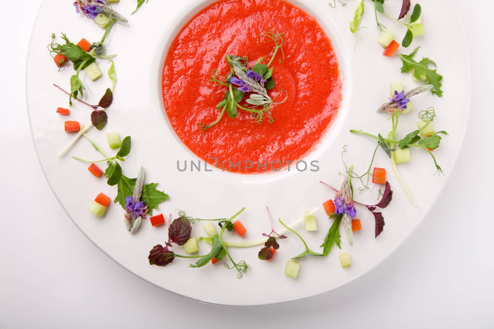 Dish filled with bright red cazpacho soup with decorated plate