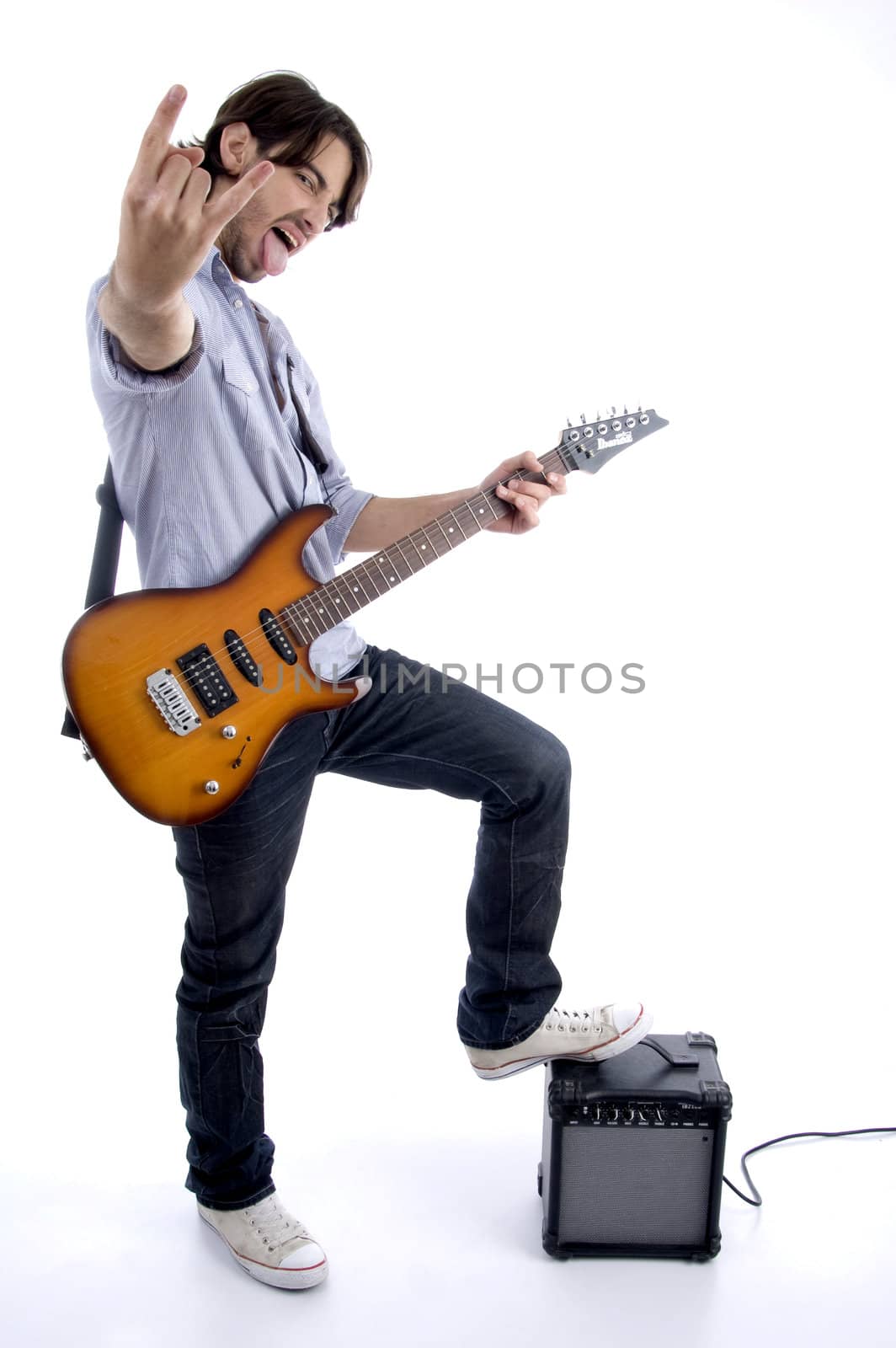 young rock star holding guitar with one leg on speaker against white background