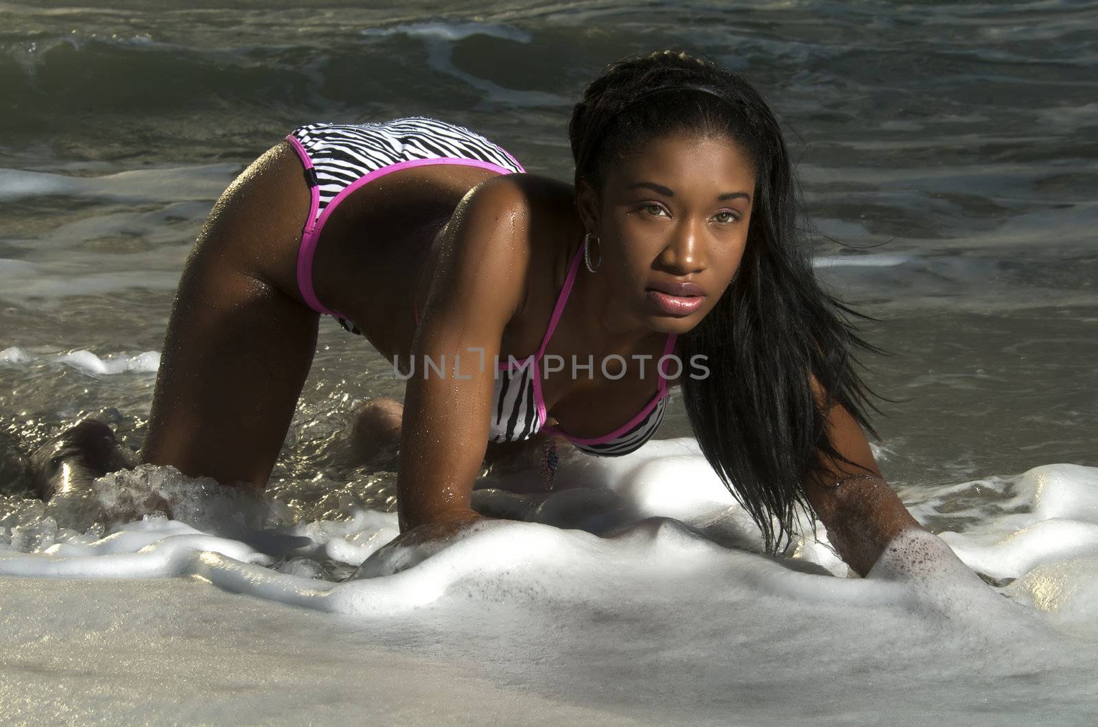 Young african american girl plays with waves in the beach.