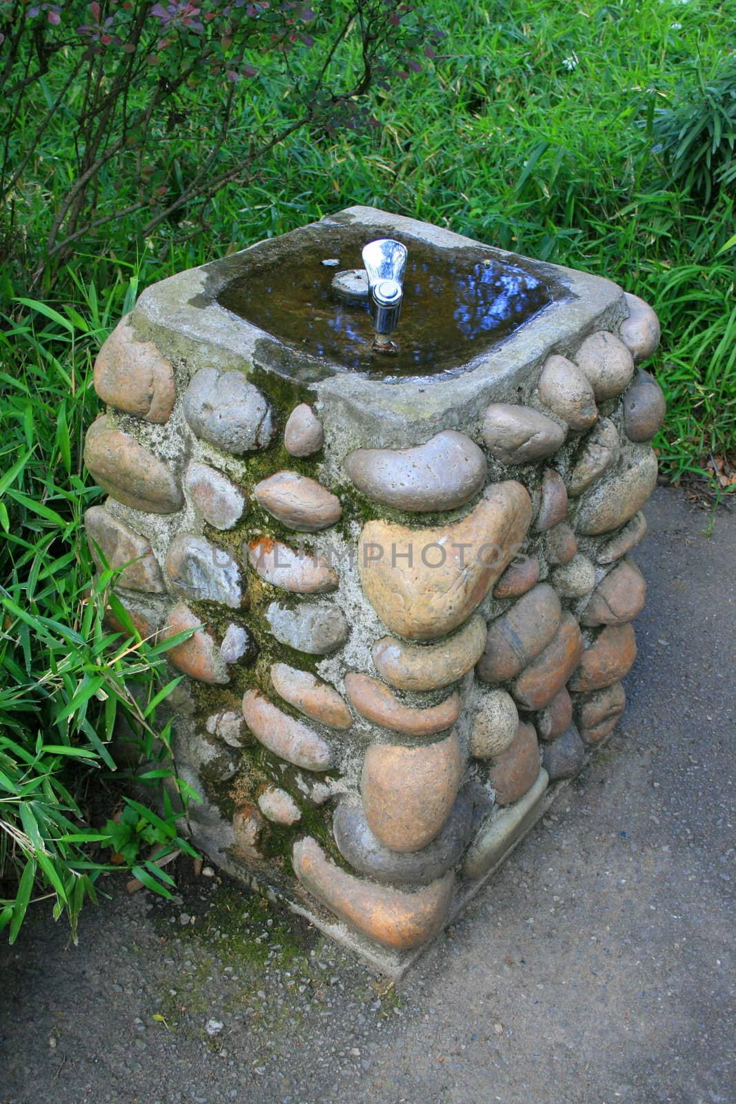 Drinking fountain on a sidewalk in a park.
