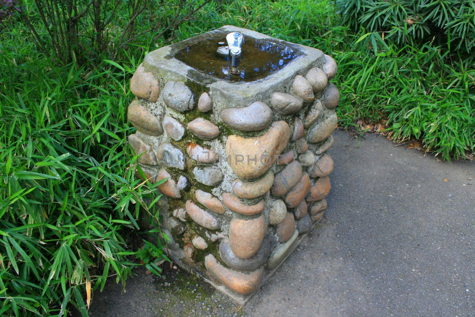 Drinking fountain on a sidewalk in a park.
