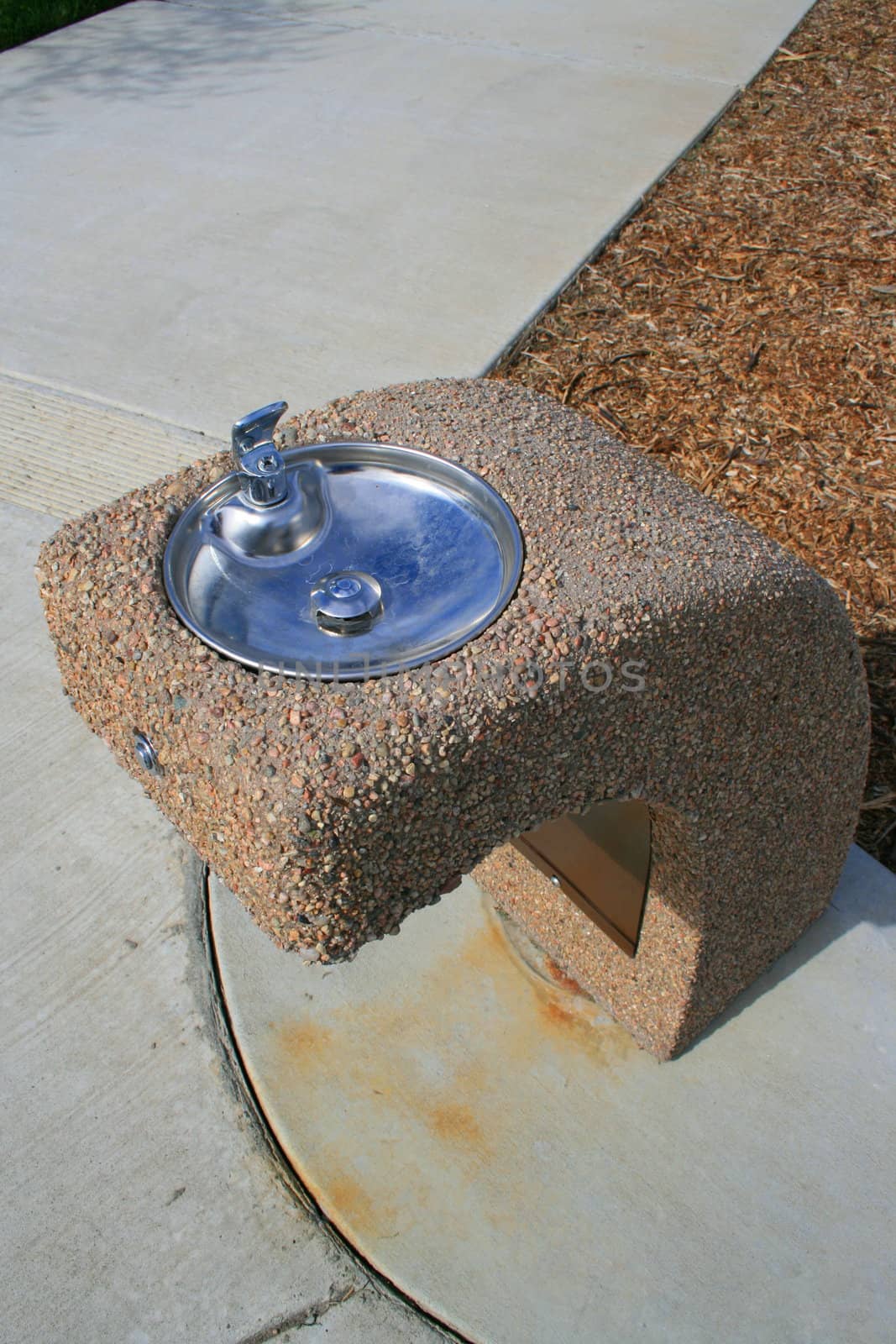 Drinking fountain on a sidewalk in a park.
