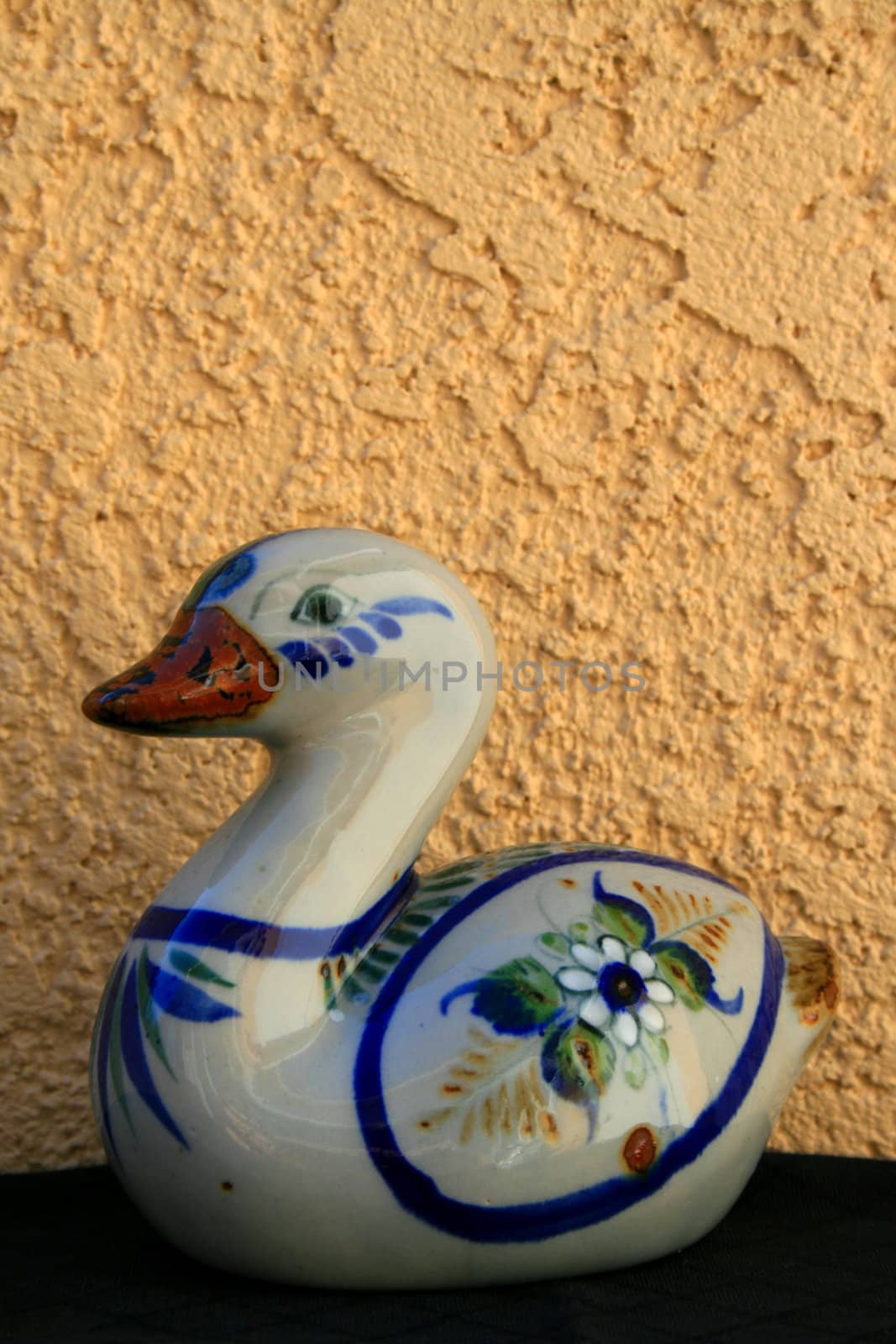 Ceramic duck figurine over cream and black background.