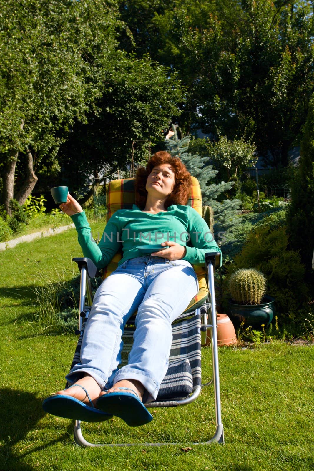 Girl relax with cap of tee in chaise longue on green grass at garden