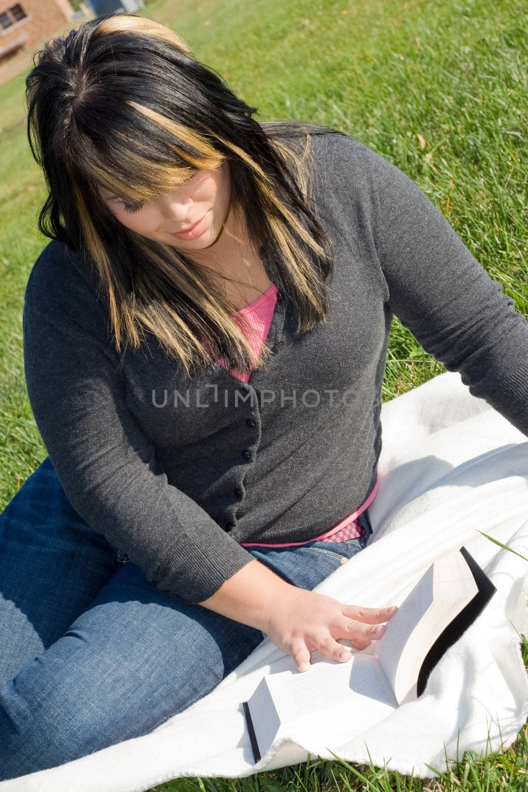 A young woman with highlighted hair reading a book or doing homework on campus.