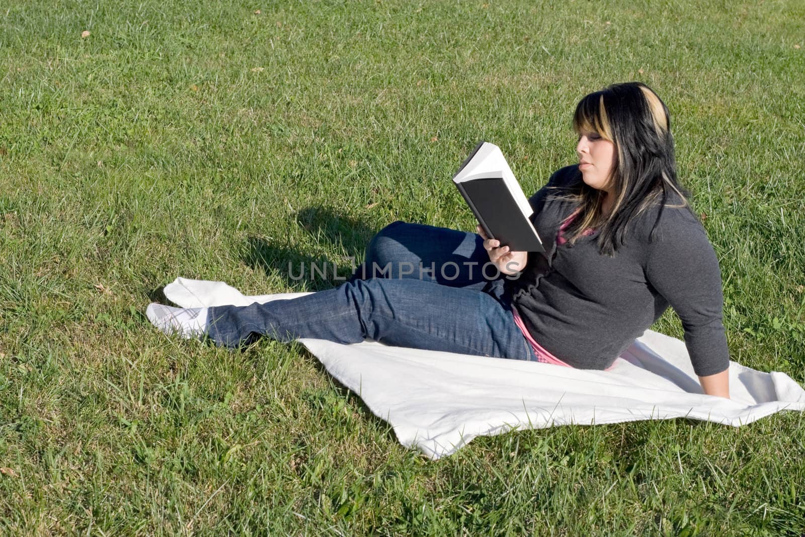 A young woman with highlighted hair reading a book or doing homework on campus.