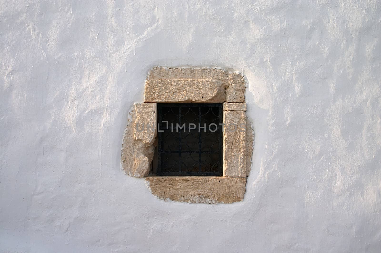 small window with grate in white lime wall