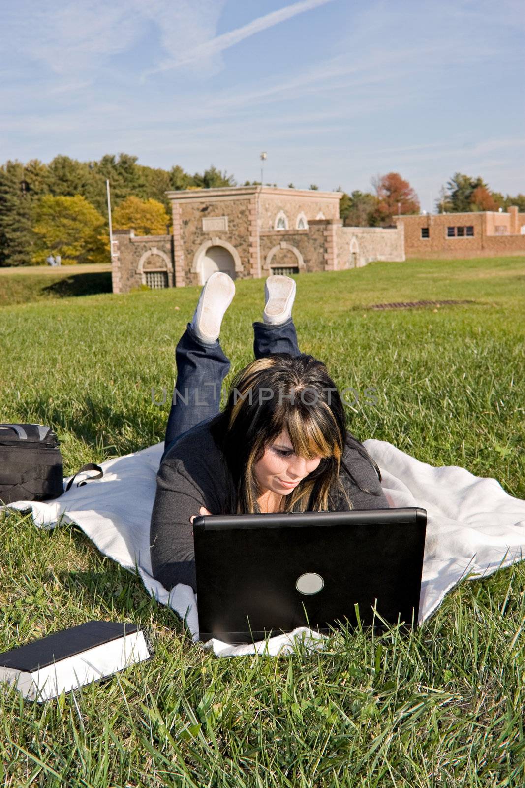 A young student using her laptop computer while laying in the grass on a nice day.