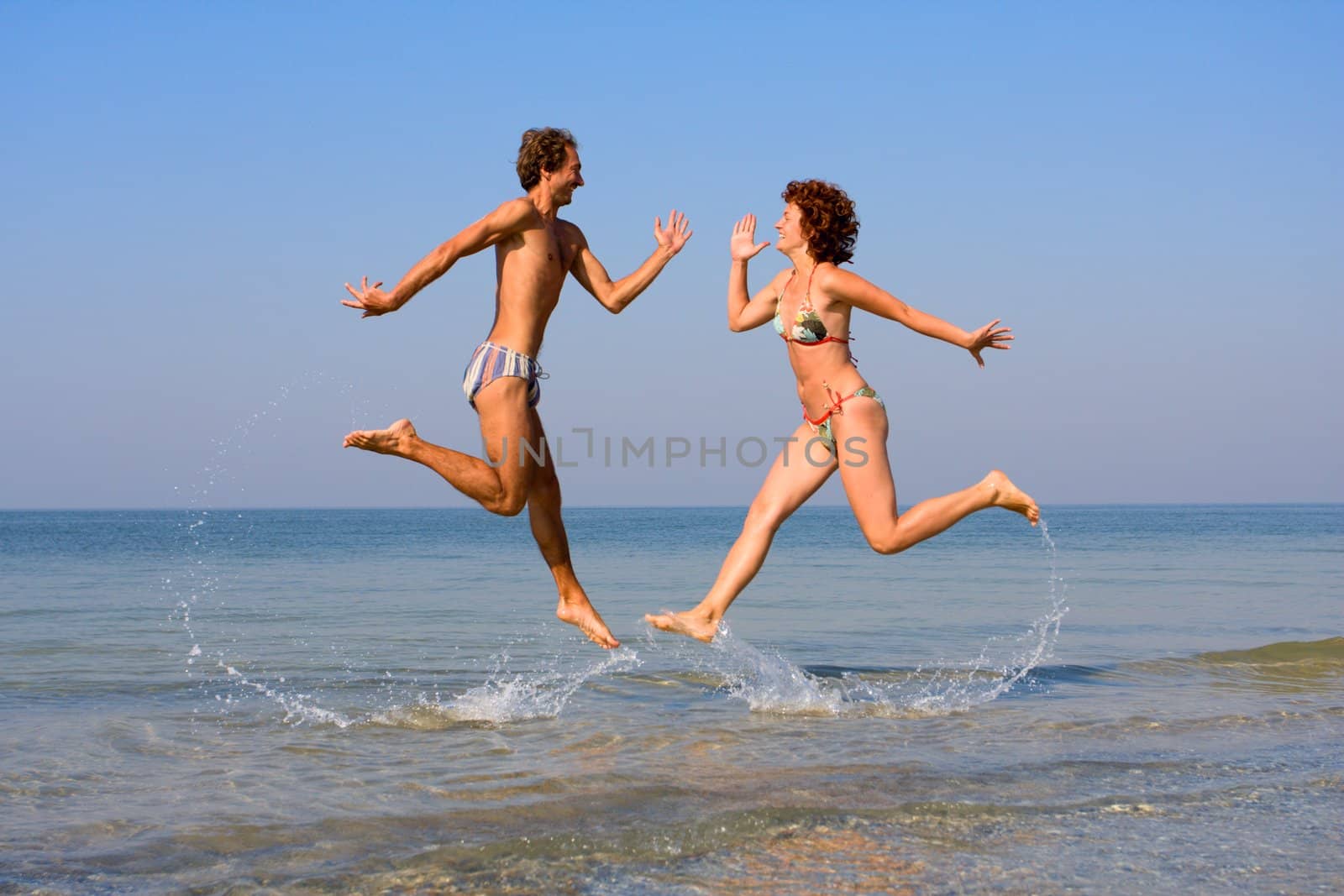 Smiling man and girl jumping at sea shoal with splashes