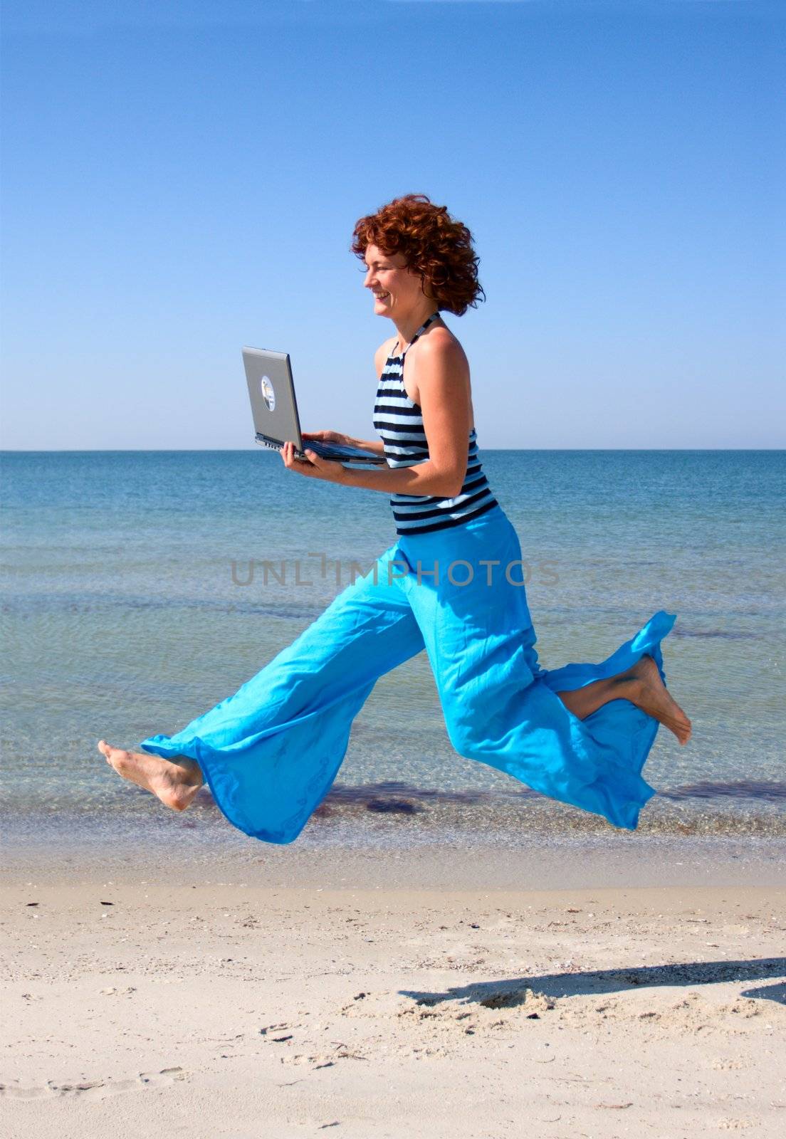 Girl with laptop running along sea beach