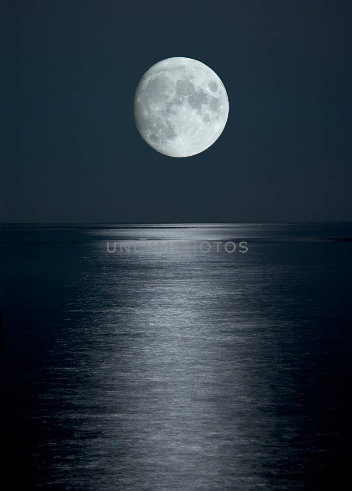 Photo of full moon in black sky above the sea with reflection