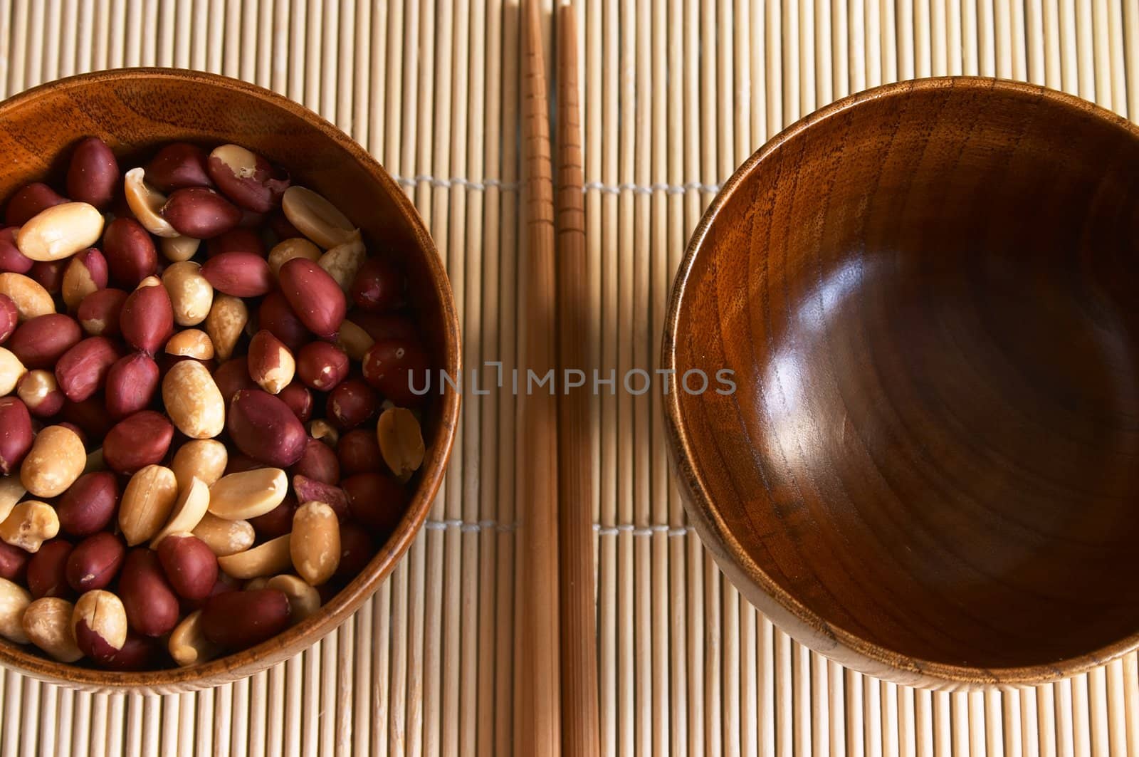 Wooden noggin with peanuts and empty one on the bamboo mat