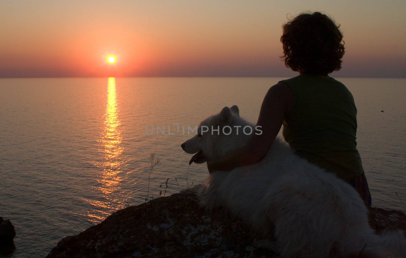 girl with dog sitting on precipice  looking to sun