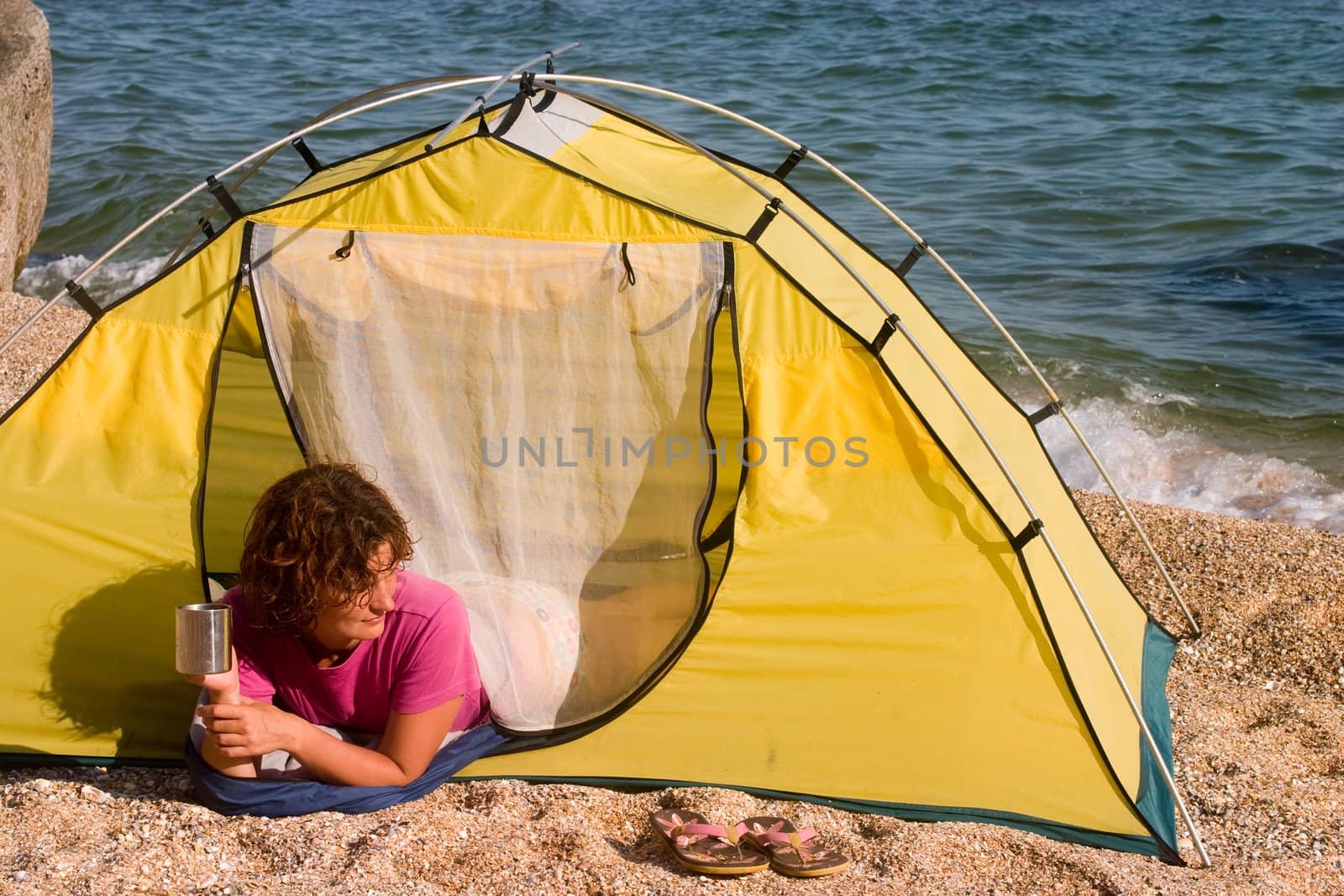 Girl with mug lying in the tent at sand sea shore