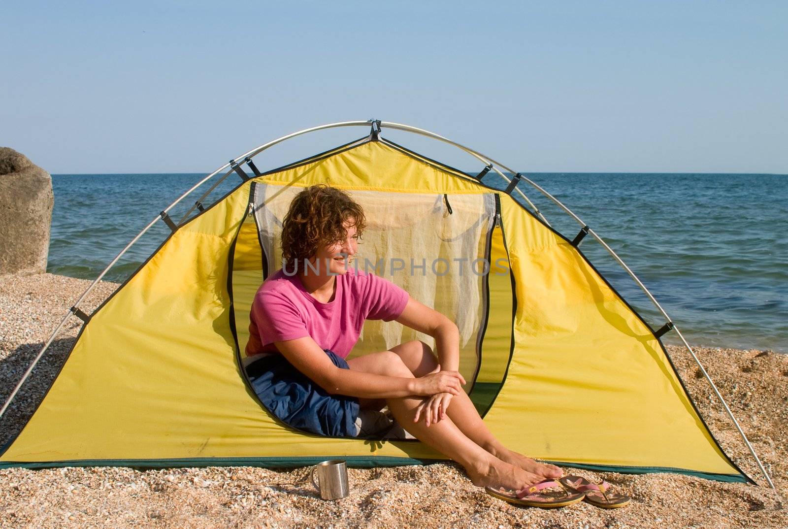 Smyling red-haired woman sitting near of tent at sea coast