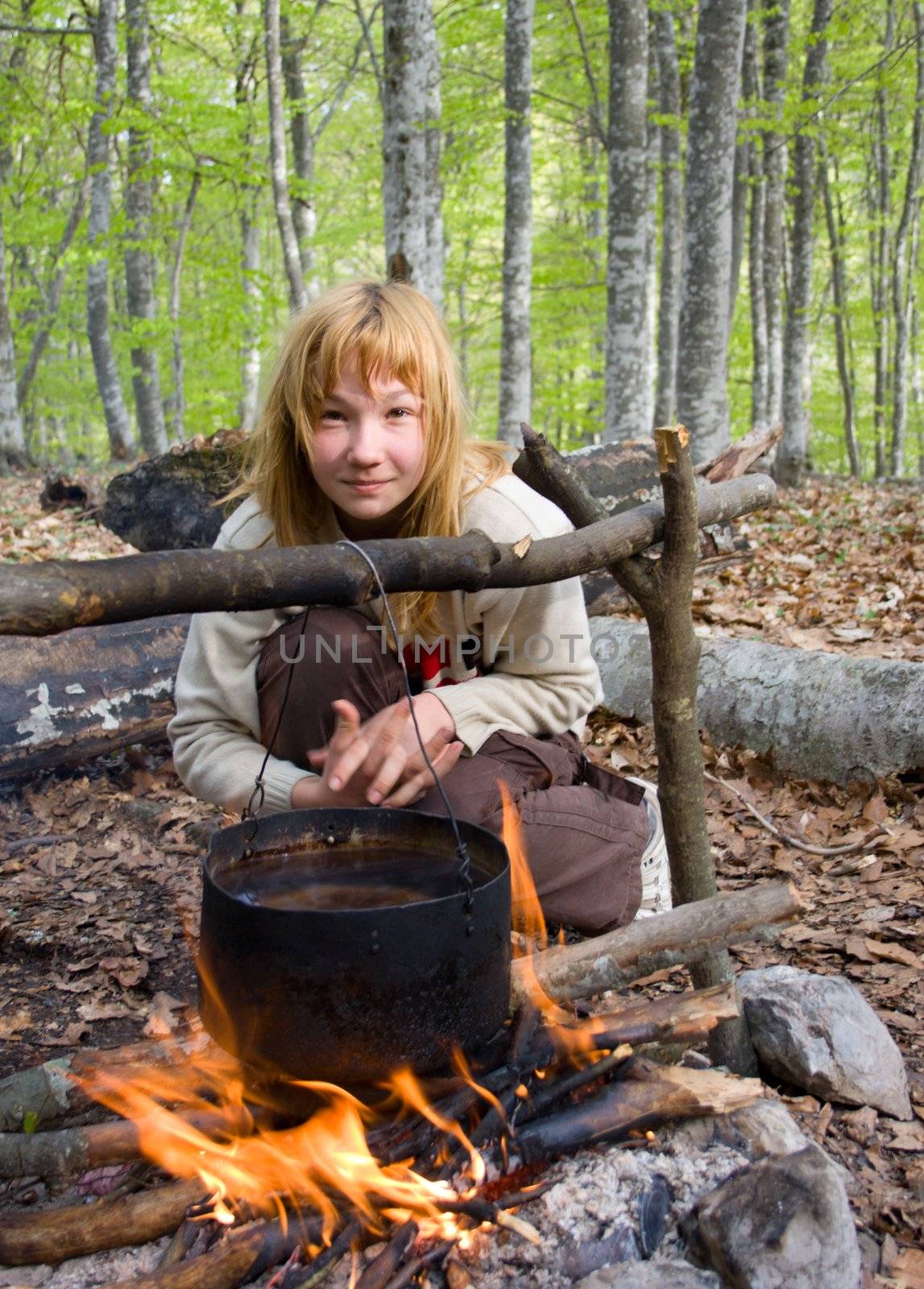 Girl sitting near of bonfire with pot in forest