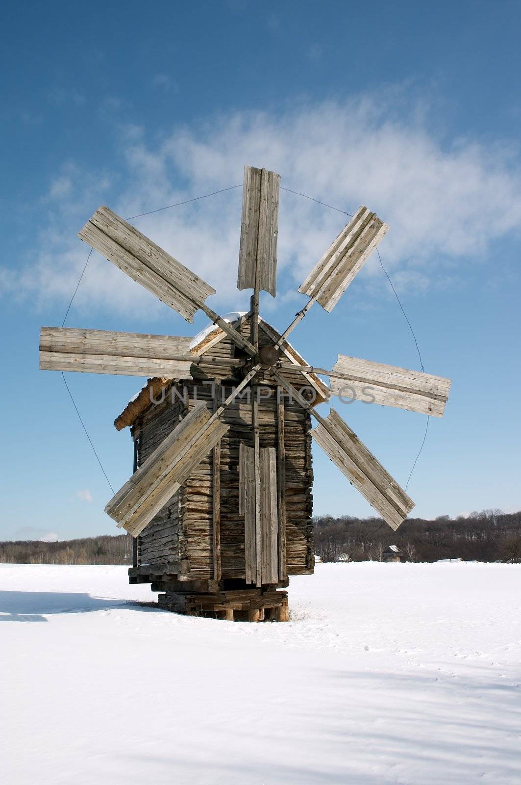 Wooden windmill on snow plain under blue sky