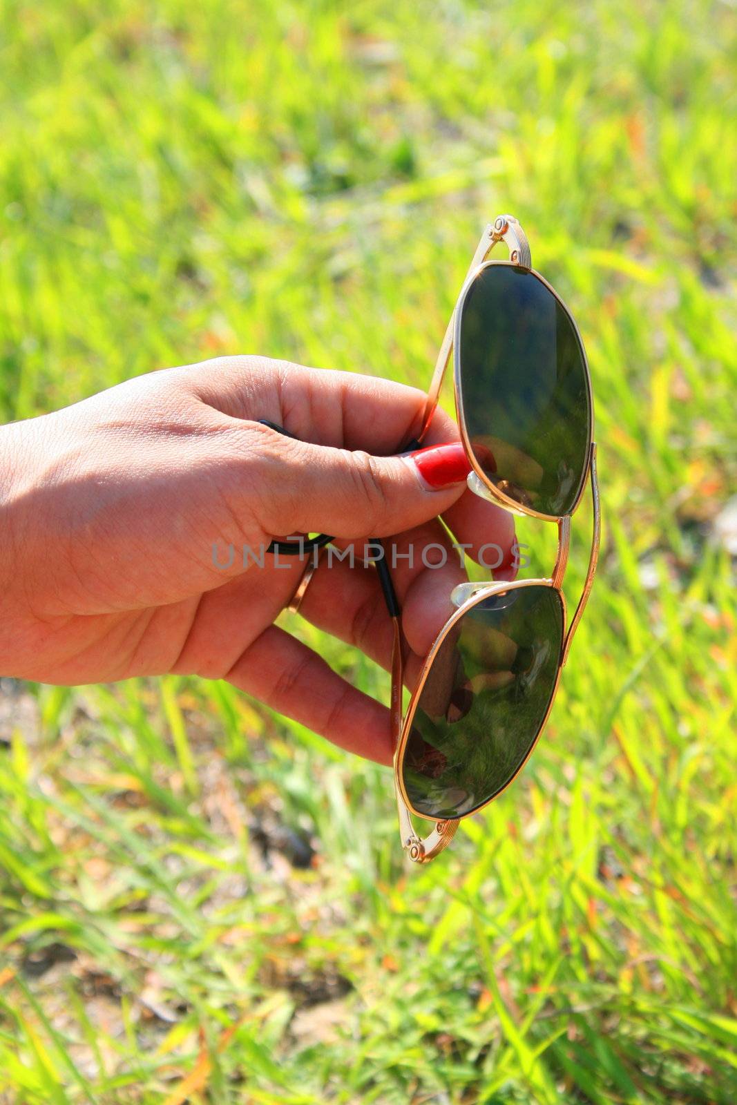 Woman's hand holding sun glasses over green grass.
