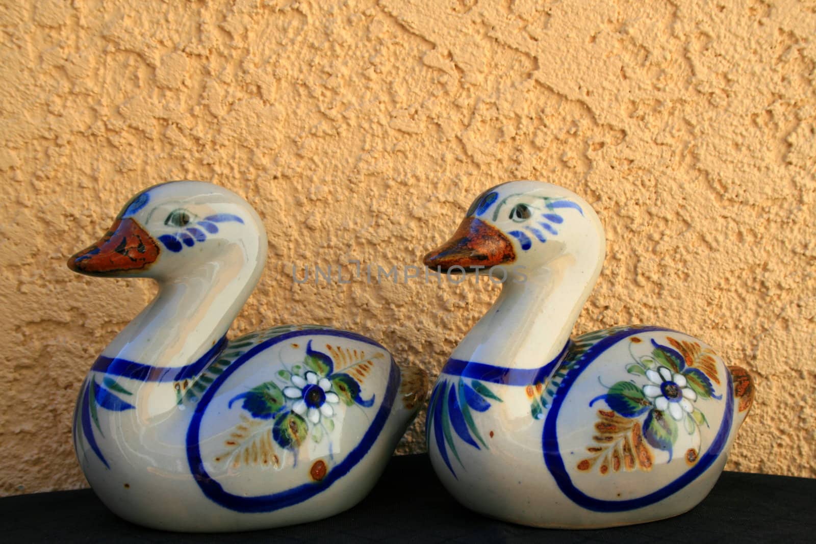 Two ceramic duck figurines over cream and black background.
