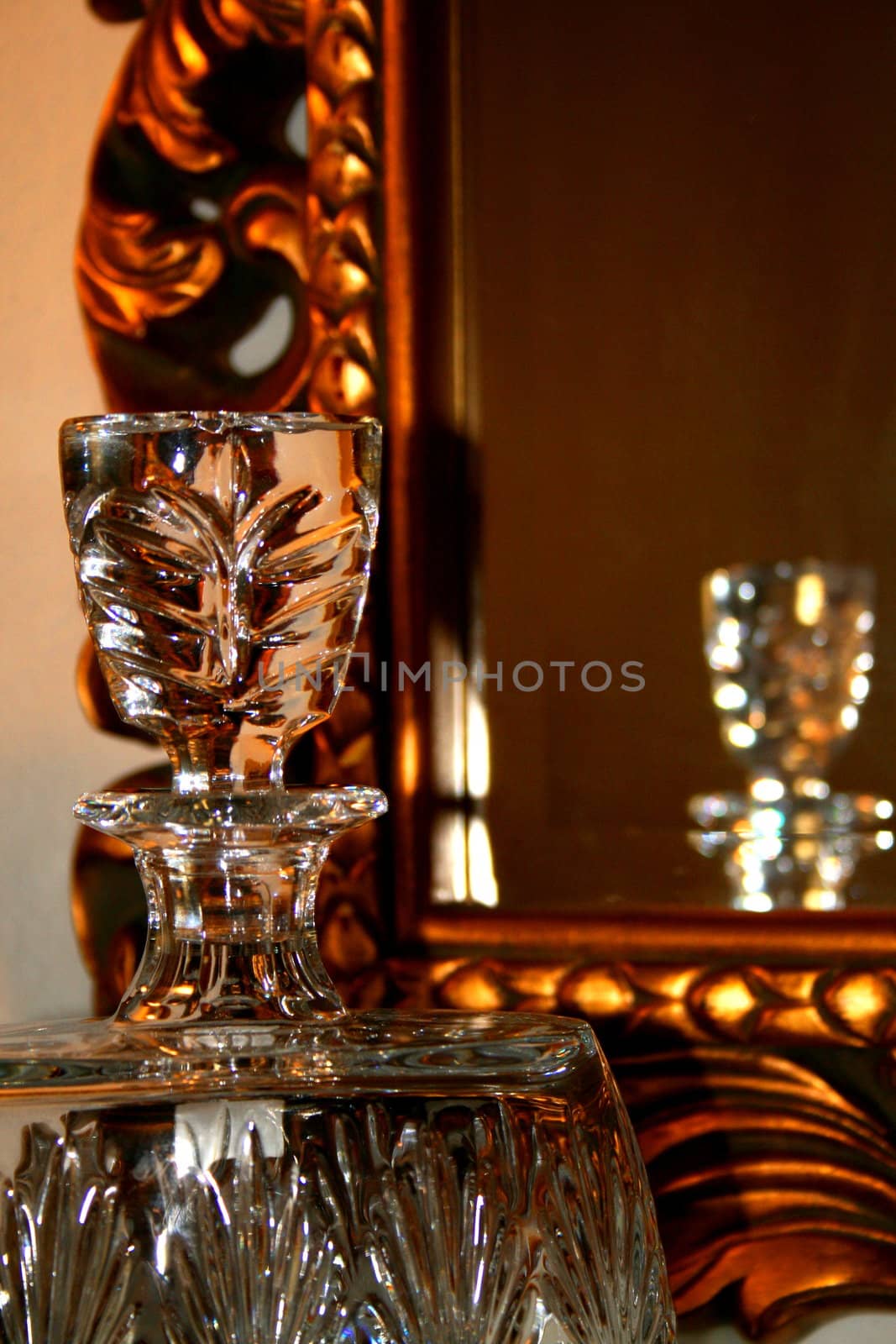 Close up of a luxury interior decor showing crystal decanter next to a mirror with a gold painted frame.
