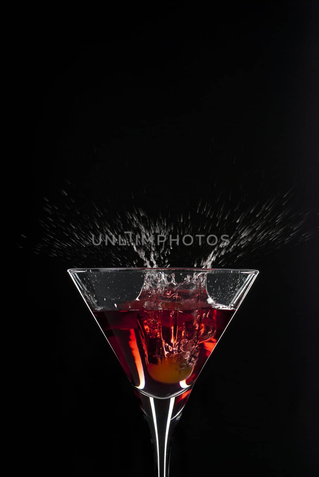 Cocktail splash with an olive on red martini with black background