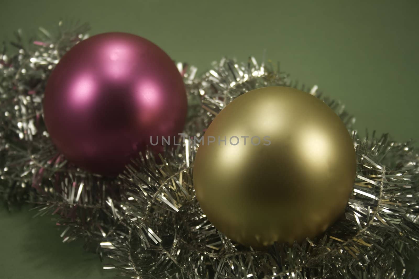 Two ornaments sitting on tinsel and isolated on green paper