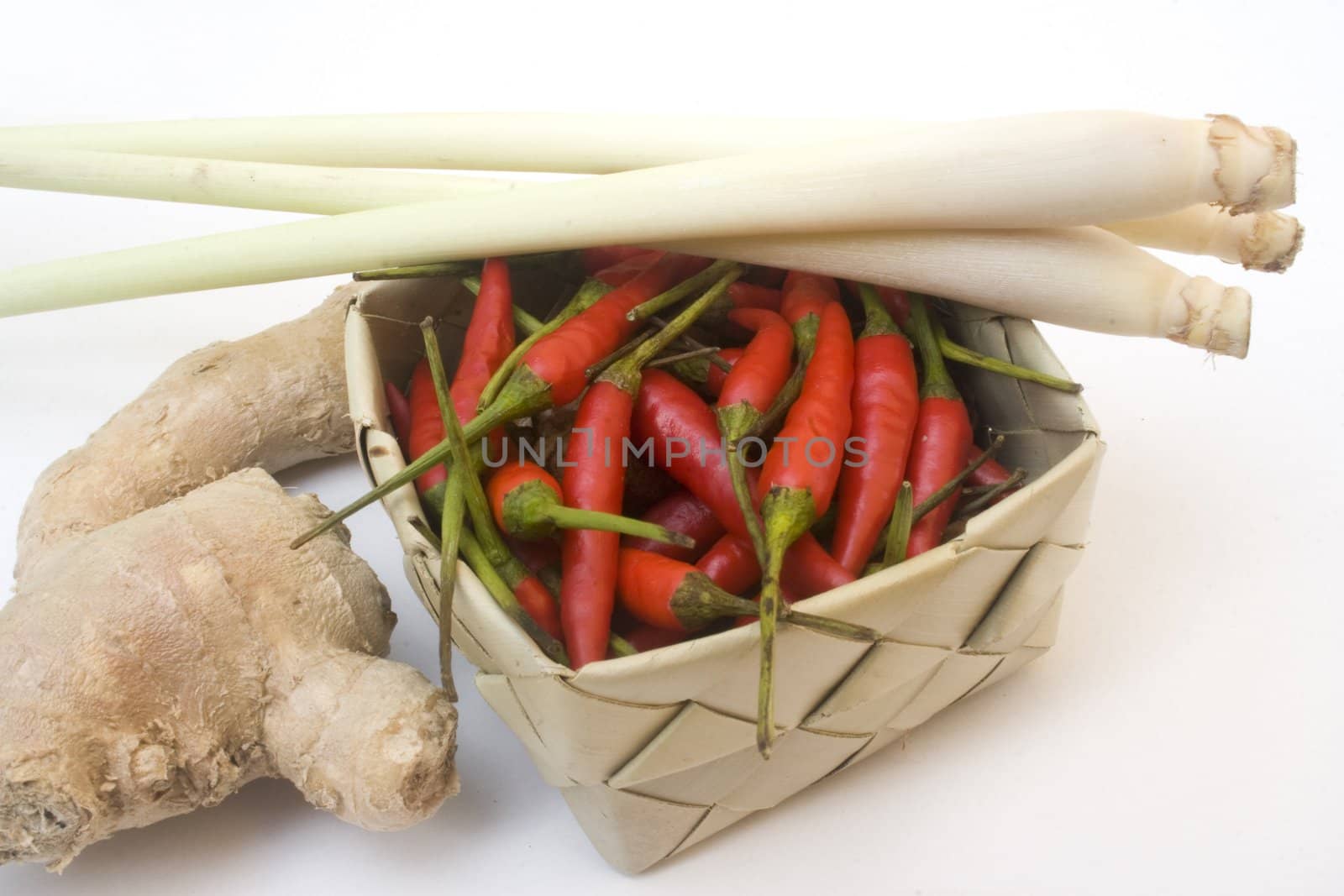 Basket of small chili peppers, ginger root, and lemon grass isolated on white