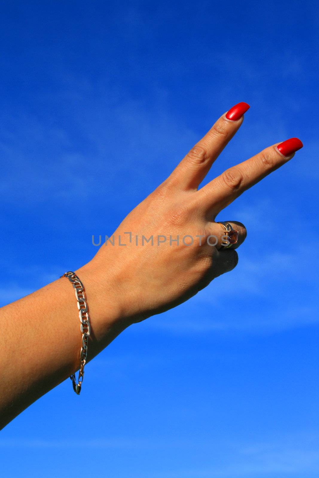 Woman's hand showing peace sign over blue sky.
