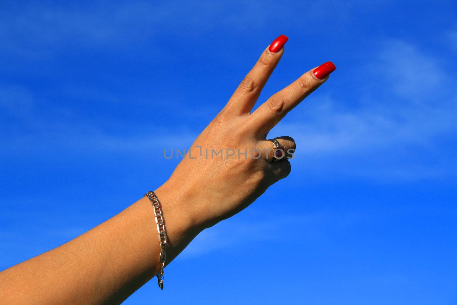 Woman's hand showing peace sign over blue sky.
