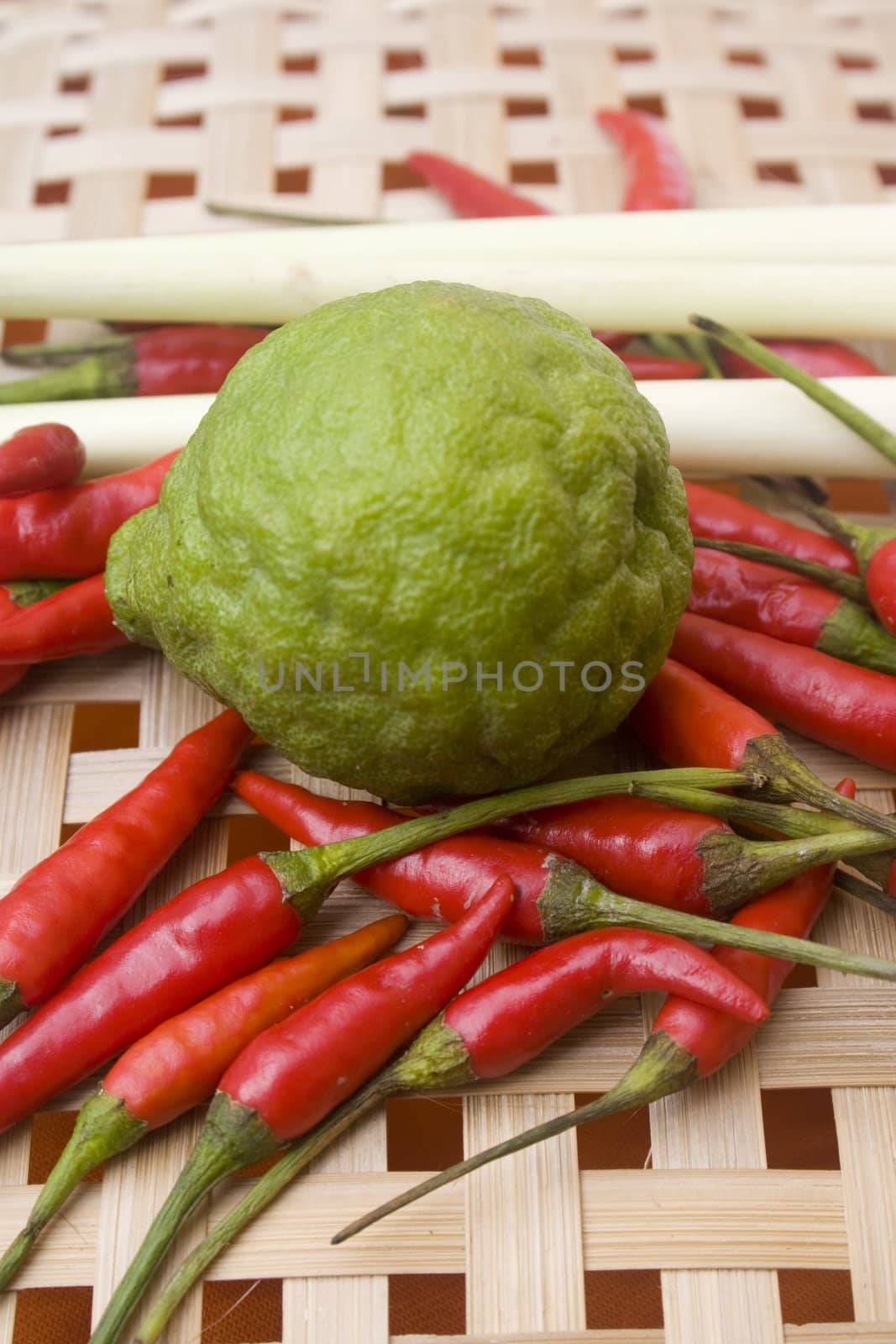 Small chili peppers, kaffir lime, galangal root, and lemon grass sitting on a woven basket