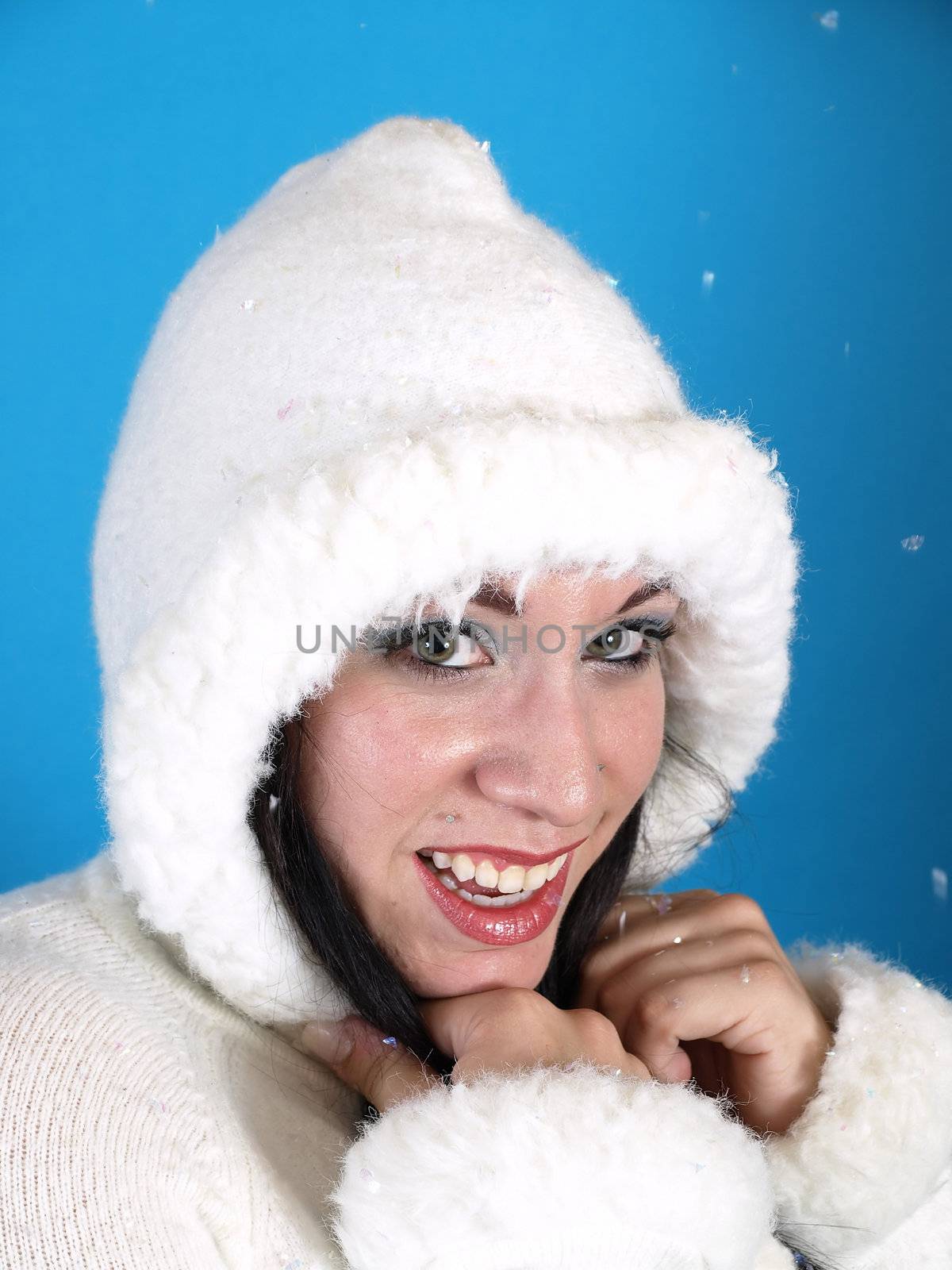 Beautiful brunette in a white hooded sweater, artificial snow falling down around her, against a blue background.