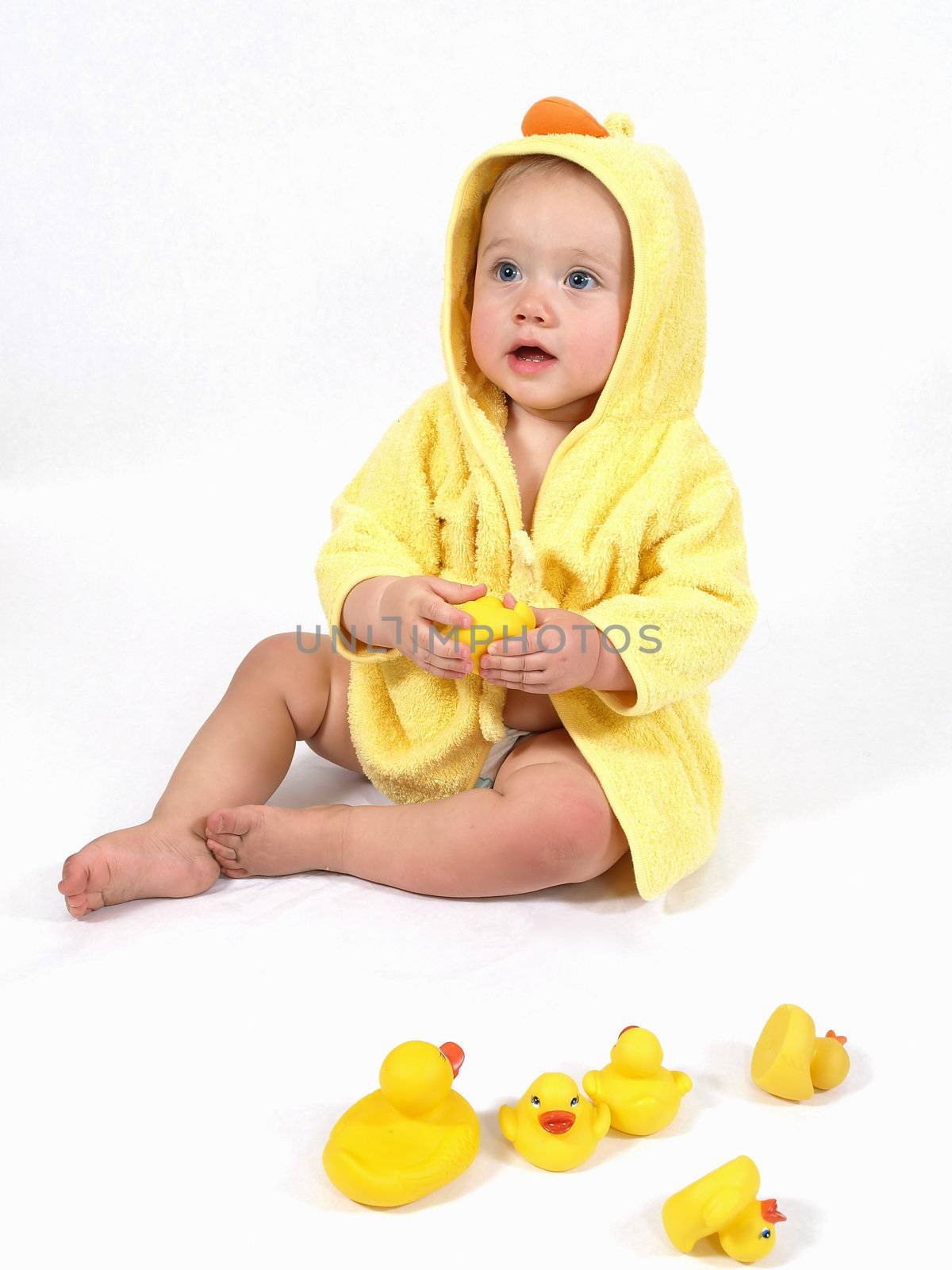 A baby girl in a yellow duck bathrobe holds a plastic toy rubber duck.