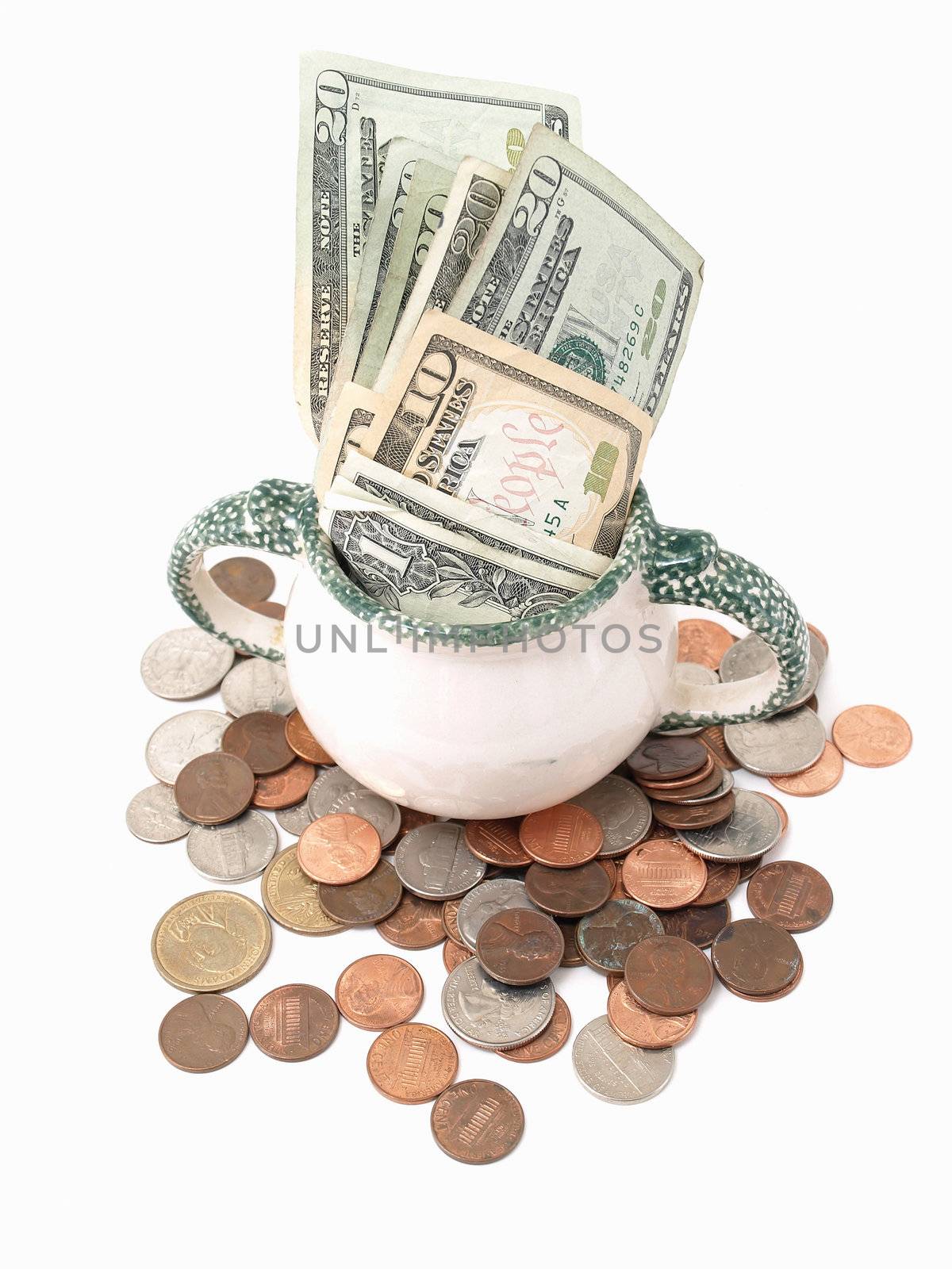 A small ceramic container holding American currency, surrounded by US coins. Over white.