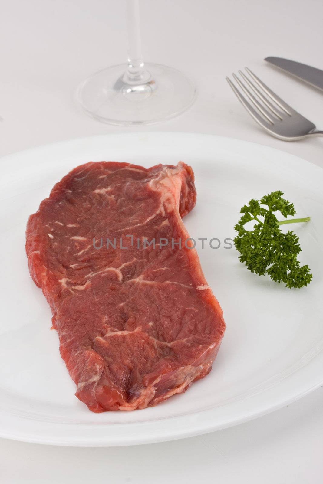 raw steak on a white plate with cutlery by bernjuer