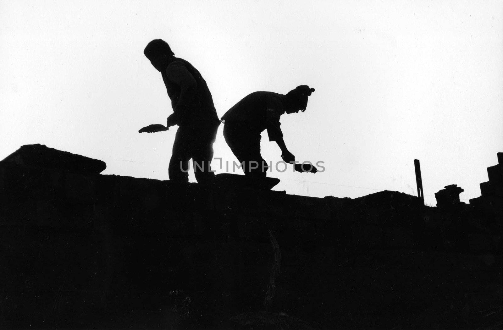two masons silhouetted as they work on the roof of a building