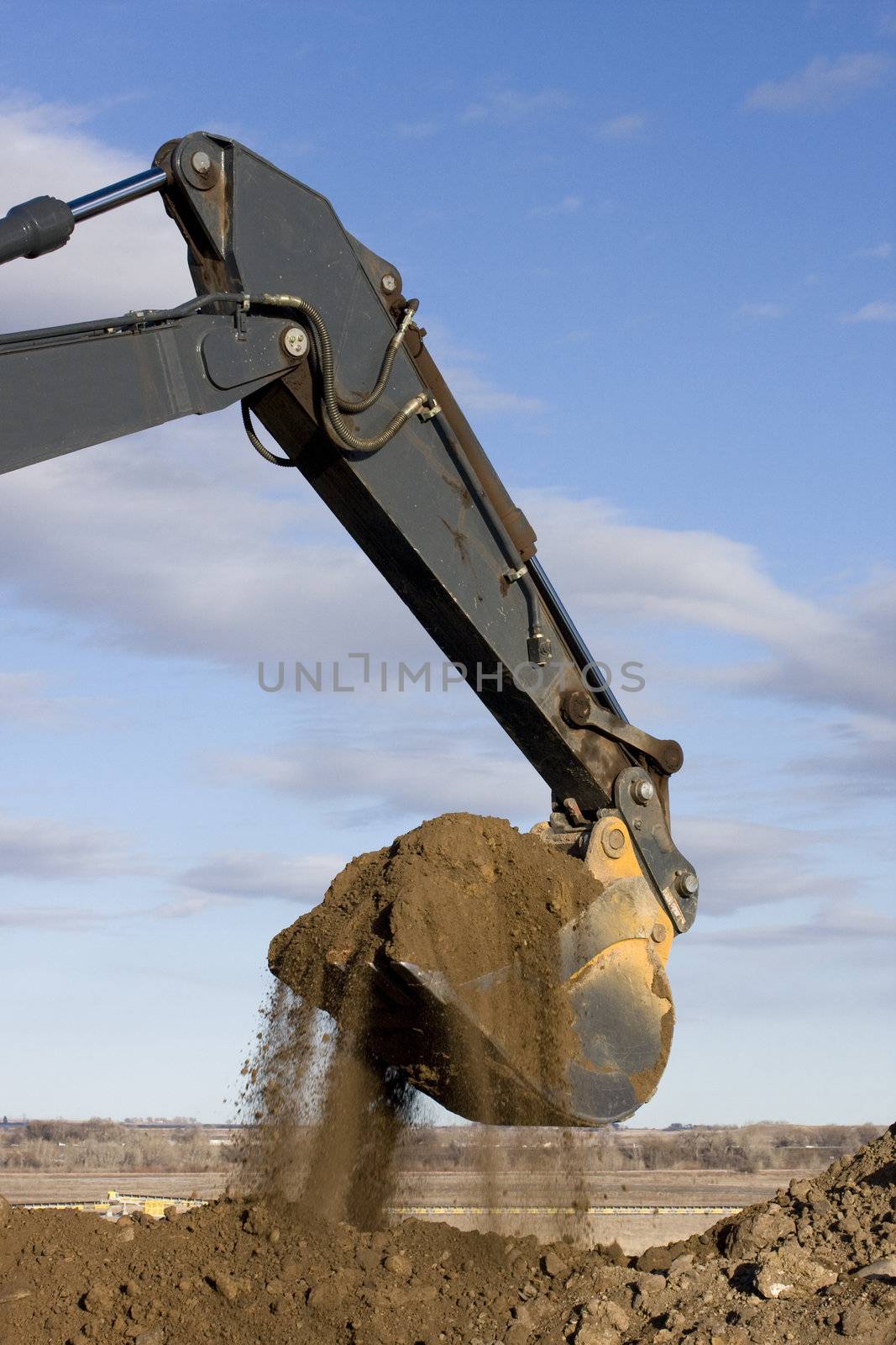 Excavator arm and scoop full of dirt at road construction against blue sky