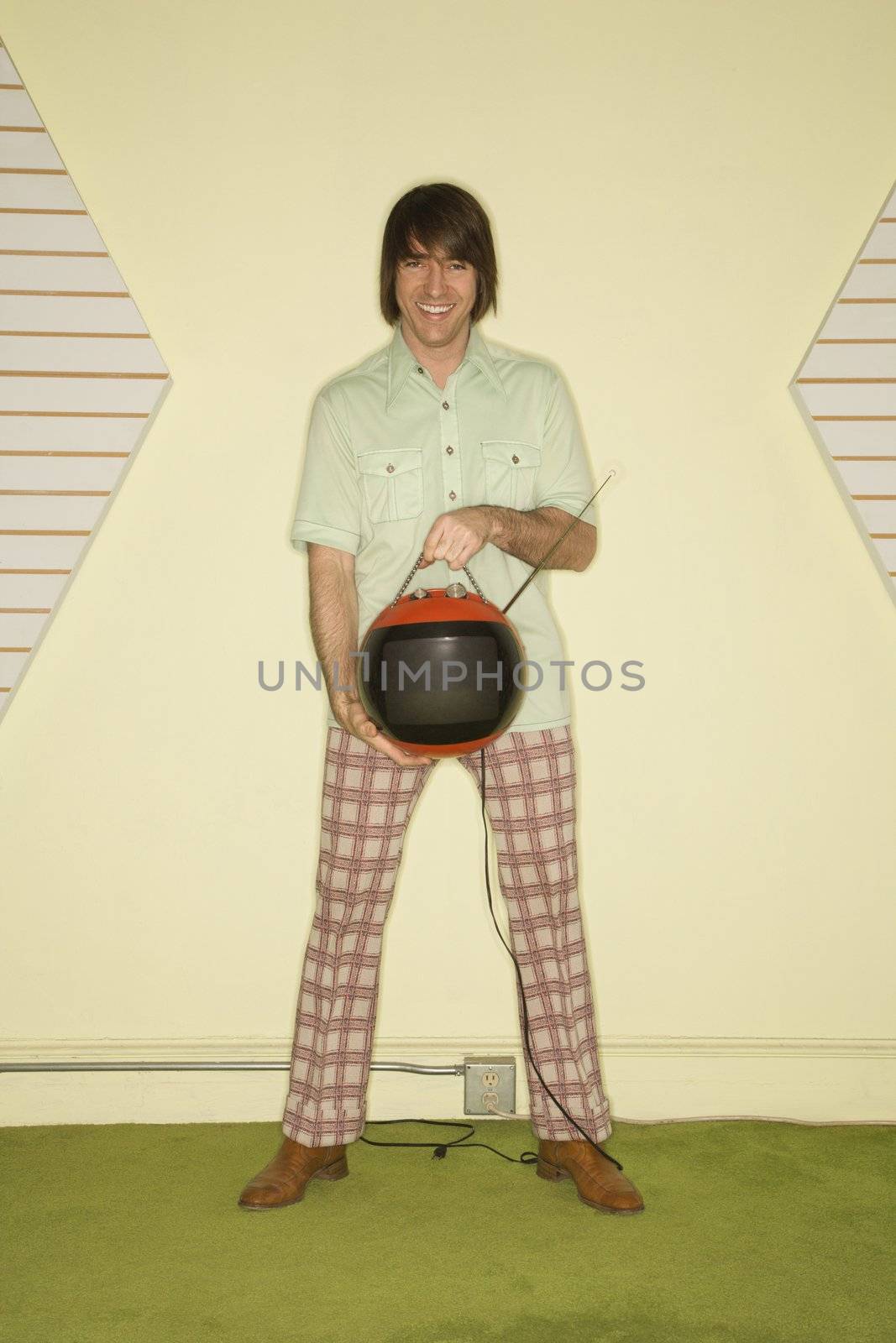 Caucasian mid-adult man wearing vintage clothing holding round red retro television.