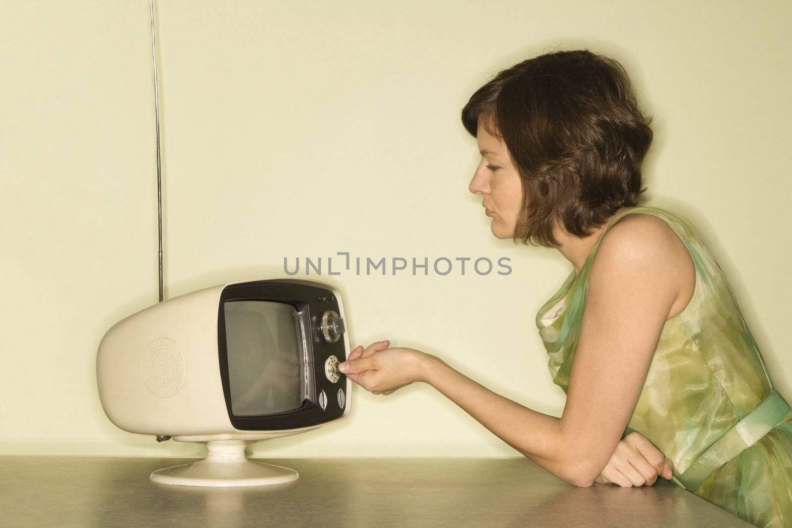 Side view of pretty Caucasian mid-adult woman sitting at 50's retro dinette set turning old televsion knob.