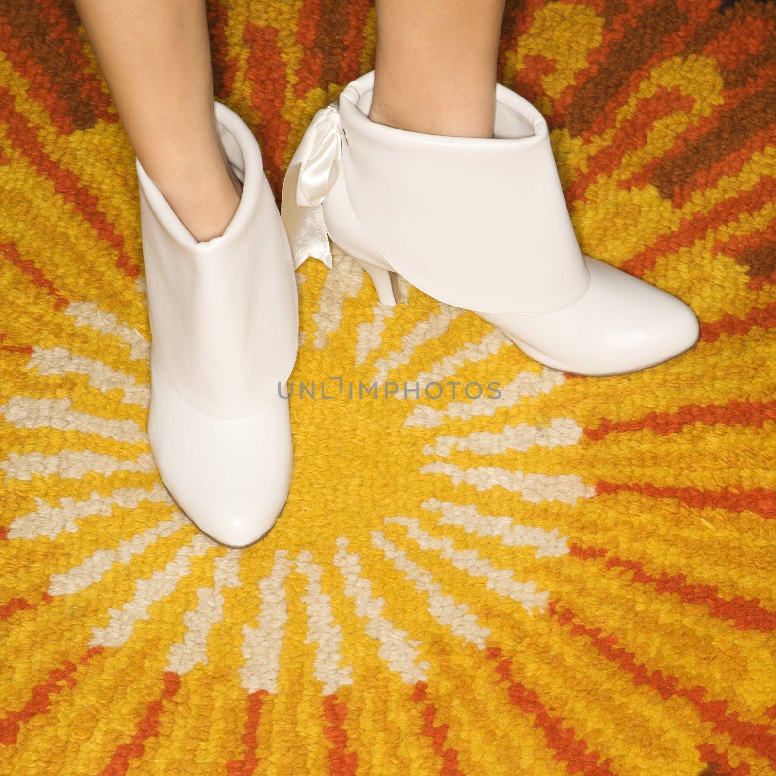 Close-up of Caucasian mid-adult female feet in white vintage boots against sunburst rug.
