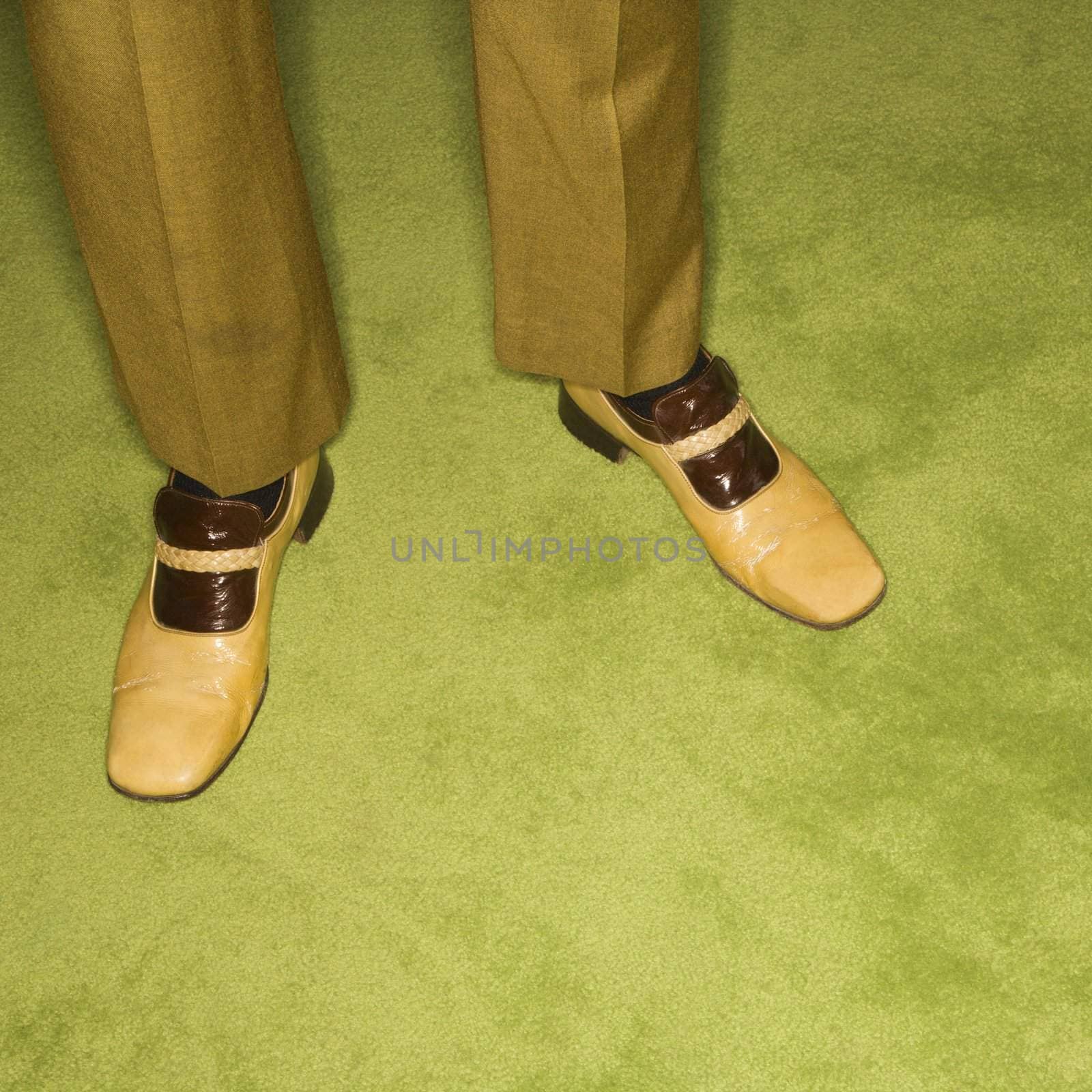 Close-up of Caucasian mid-adult male feet in vintage shoes against green rug.