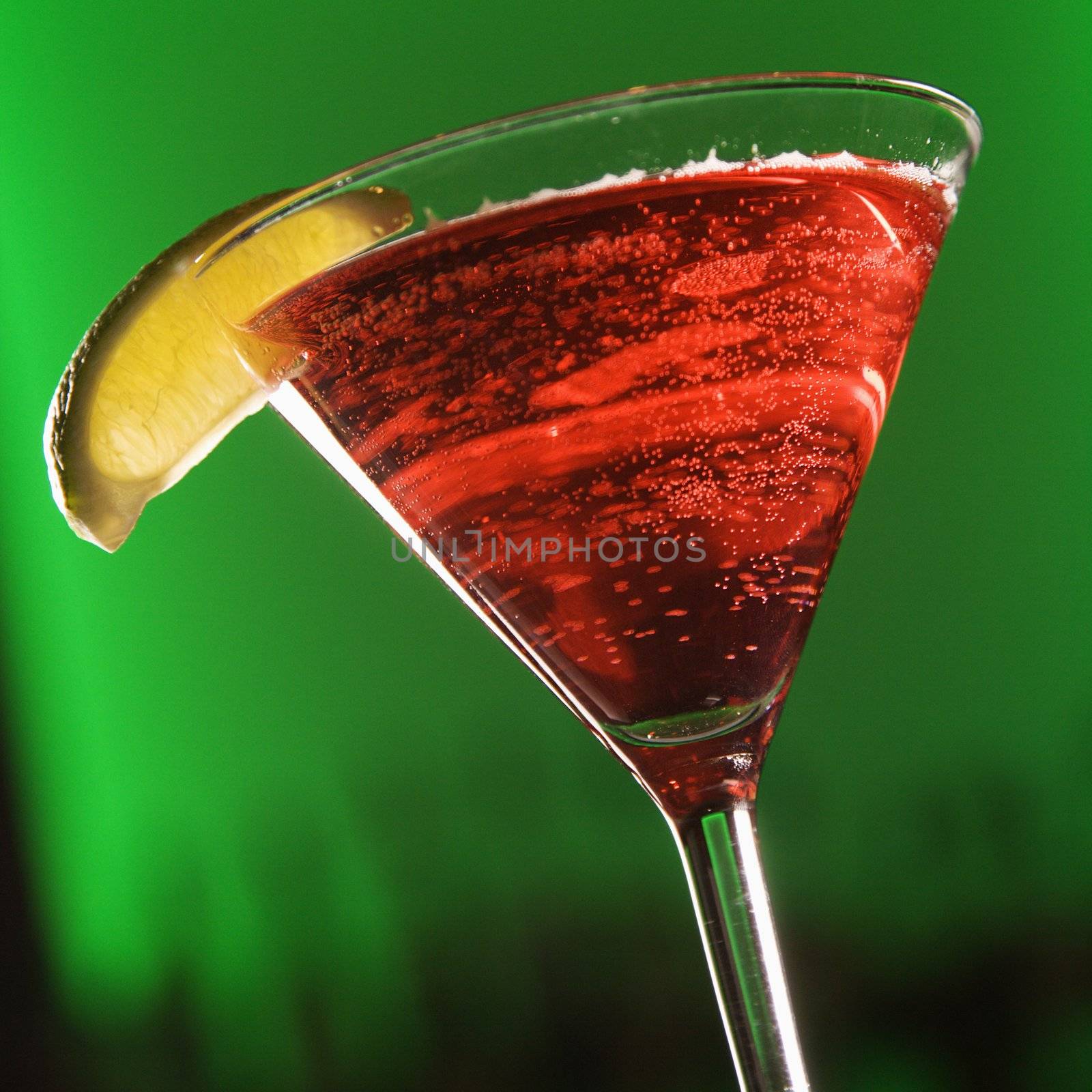 Still life of martini cocktail with fruit garnish against glowing green background.