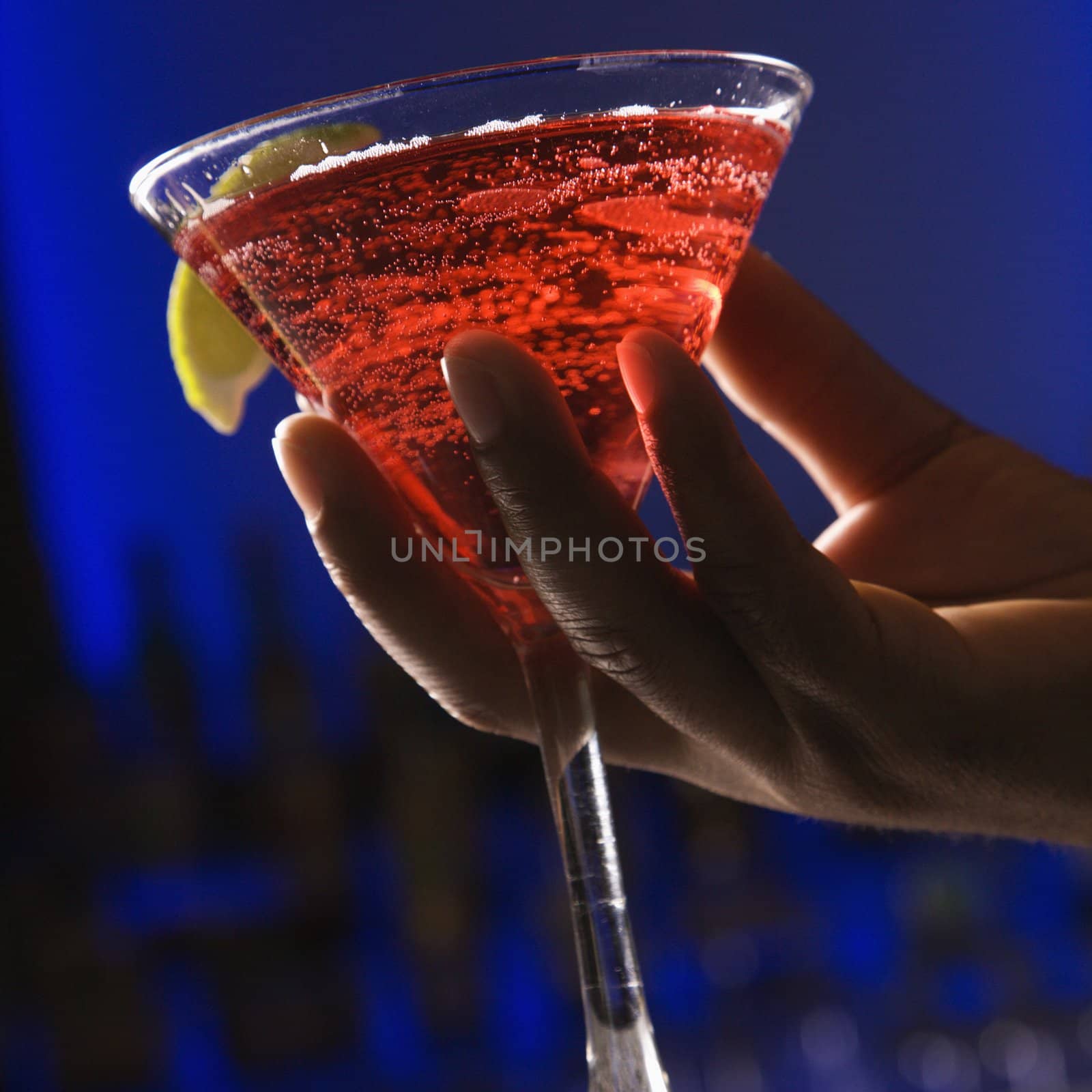 African American male hand holding martini in bar against glowing blue background.