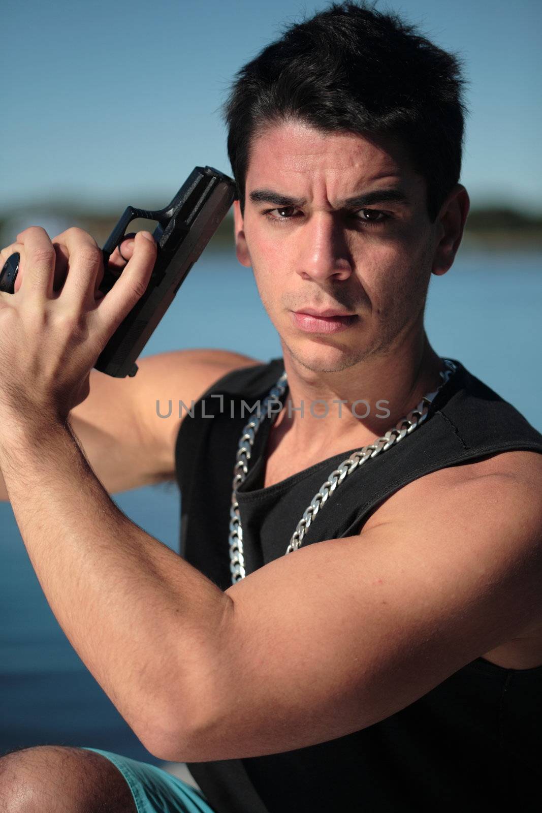 A young man, wearing a sleeveless shirt, holding a hand gun. (This image is part of a series)