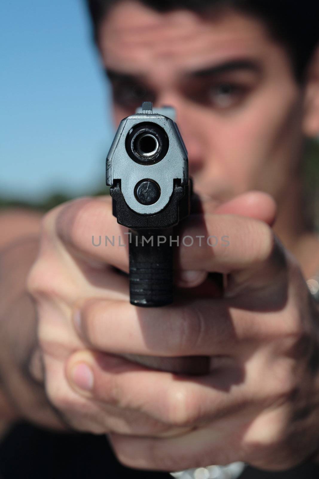 A young man, wearing a sleeveless shirt, holding a hand gun. (This image is part of a series)